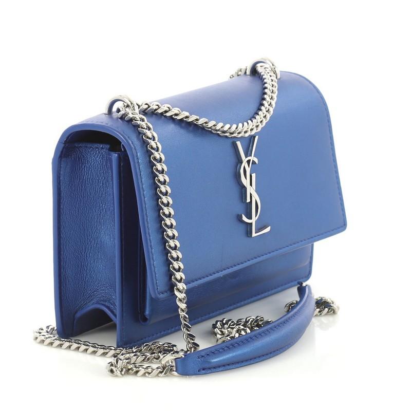 This Saint Laurent Sunset Chain Wallet Leather, crafted from blue leather, features YSL monogram logo at the front, sliding chain-link shoulder strap, and silver-tone hardware. Its magnetic snap closure opens to a black leather interior with zip