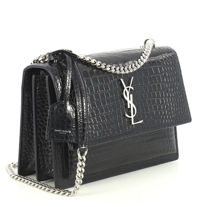 This Saint Laurent Sunset Crossbody Bag Crocodile Embossed Leather Medium, crafted in blue crocodile embossed leather, features chain link strap, accordion sides and silver-tone hardware. Its magnetic snap button closure opens to a blue suede