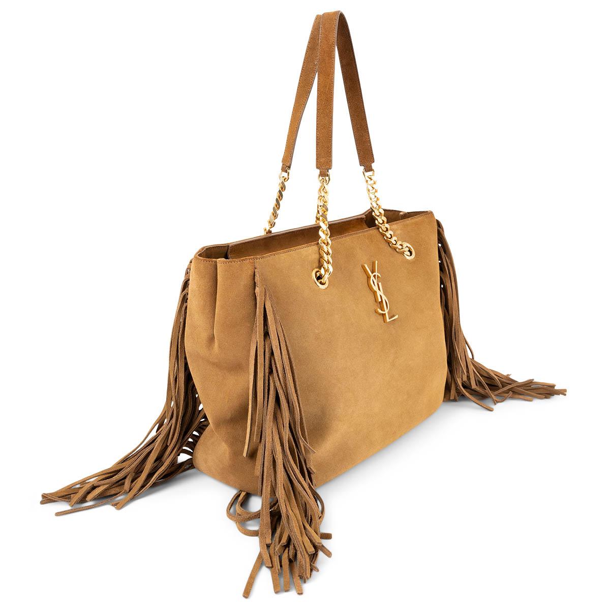 100% authentic Saint Laurent shopper bag in tan suede leather featuring gold-tone hardware. The design comes with fringe trim on the side, shoulder straps with curb-chain insets and a gold-tone glossy monogram logo on the front. Opens with a zipper