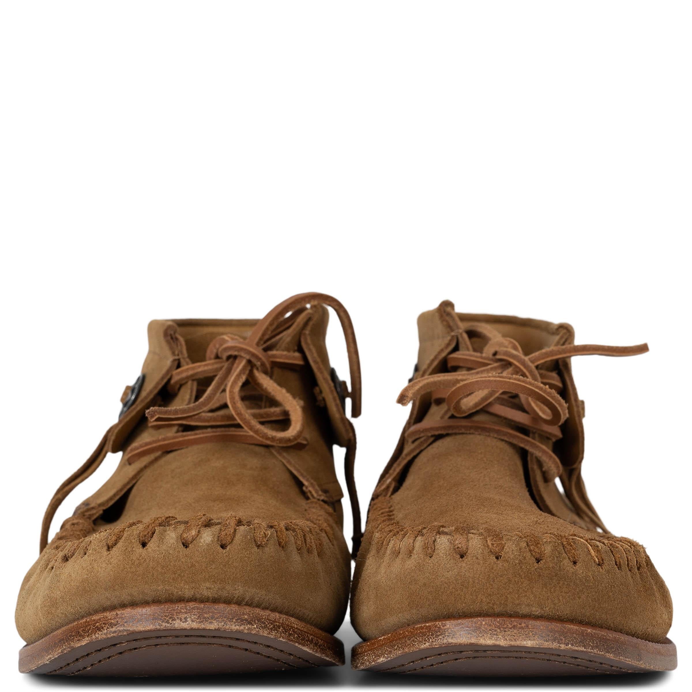 This 100% authentic Saint Laurent Mocassin Desert ankle boots in tan suede capture a bohemian spirit with a luxe edge. Embellished with conchos and fringe, they feature round toes with intricate whipstitching on the front upper. A perfect fusion of