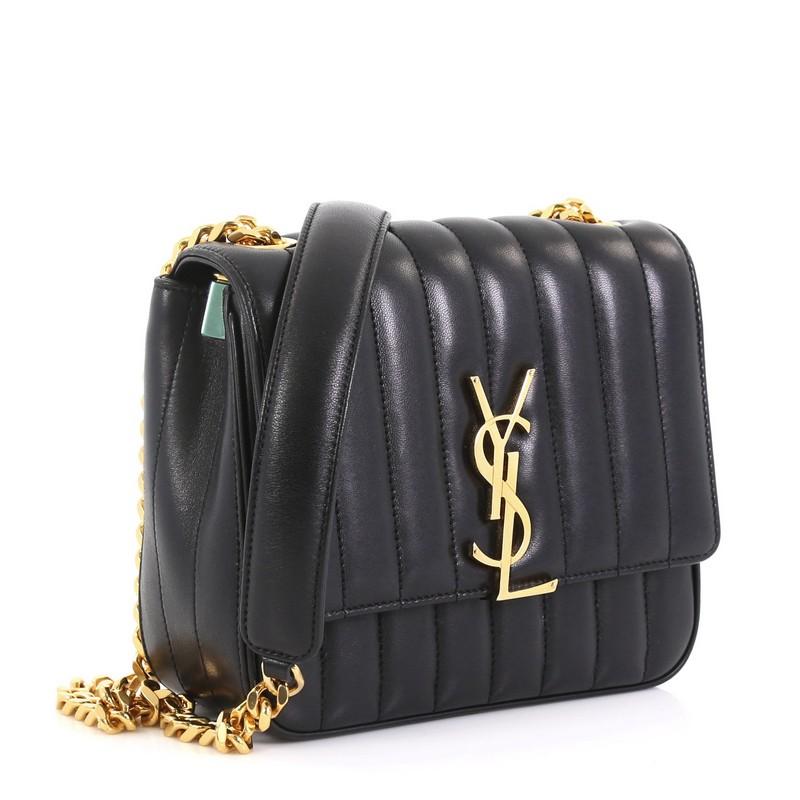 This Saint Laurent Vicky Crossbody Bag Vertical Quilted Leather Medium, crafted in black vertical quilted leather, features a chain link strap, signature interlocking YSL logo at its center, and gold-tone hardware. Its magnetic snap closure opens to