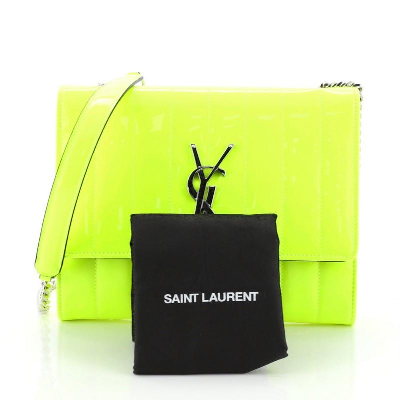 This Saint Laurent Vicky Crossbody Bag Vertical Quilted Patent Medium, crafted in yellow vertical quilted patent leather, features a chain link strap, interlocking YSL logo at its center, and silver-tone hardware. Its magnetic snap closure opens to
