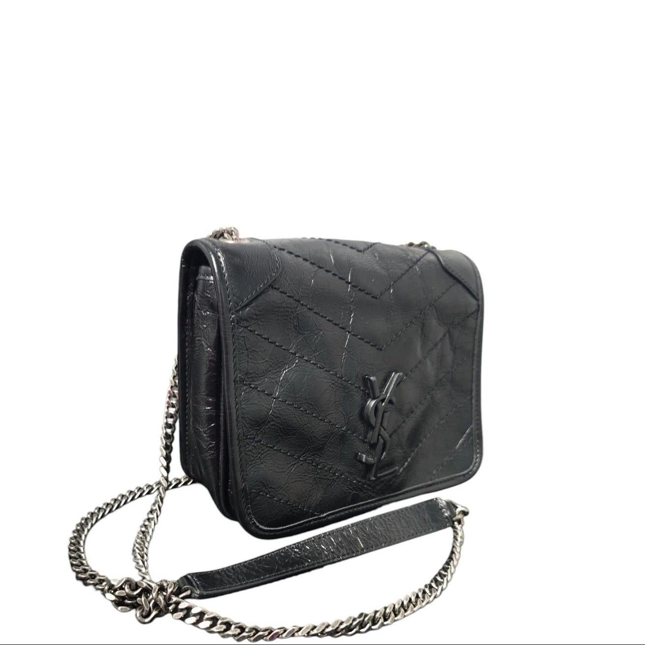 Faites l'expérience de l'élégance intemporelle avec le portefeuille Niki d'YSL Saint Laurent sur chaîne. Confectionné en luxueux cuir de veau froissé noir à chevrons et orné de ferrures en argent vieilli, ce portefeuille conçu en Italie présente une