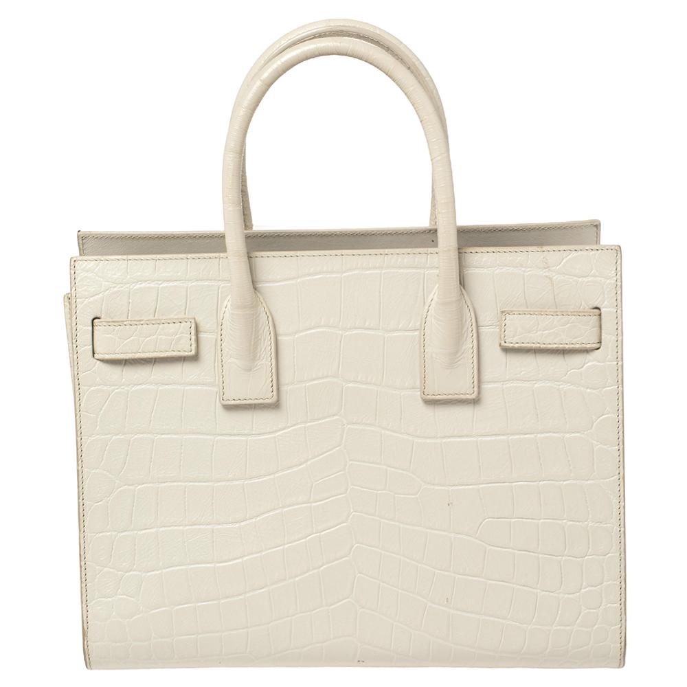 This Sac de Jour tote by Saint Laurent has a structure that simply spells sophistication. Crafted from white croc-embossed leather, the bag is held by double top handles. The tote comes with a leather-lined interior with enough space to store your