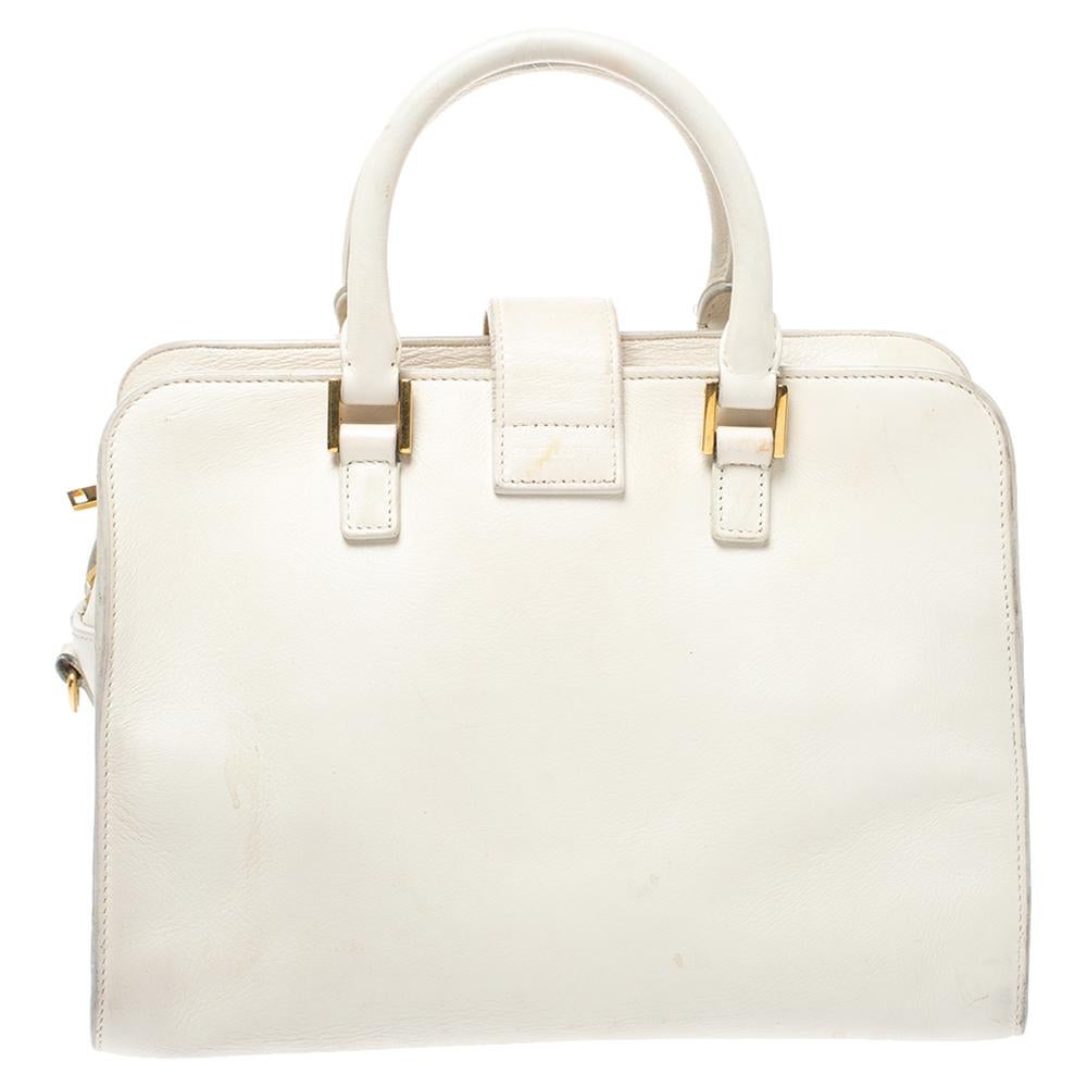 This subtle, white Cabas tote from Saint Laurent Paris is ideal for everyday use. Crafted from leather, the bag is detailed with a gold-tone YSL motif snap closure, dual leather handles, a shoulder strap, a leather tag, and protective metal feet at