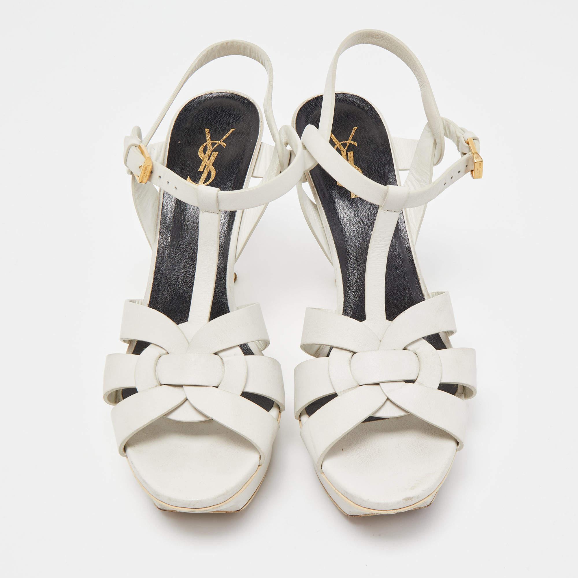 The fashionista in you will instantly fall in love with these Saint Laurent Tribute sandals! They are made from white leather with intertwined straps on the vamps and ankle buckle closure. The gold-tone hardware, 12cm heels, and platforms give it a