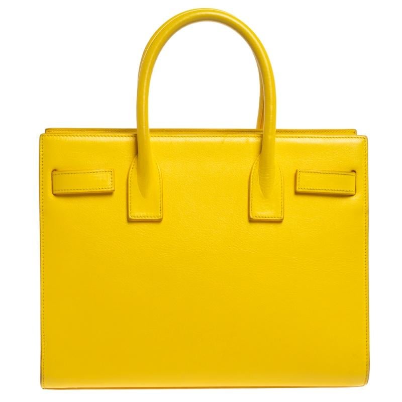 This Sac de Jour tote by Saint Laurent has a structure that simply spells sophistication. Crafted from yellow leather, the bag is held by double top handles. The tote comes with a fabric-lined interior with enough space to store your necessities and