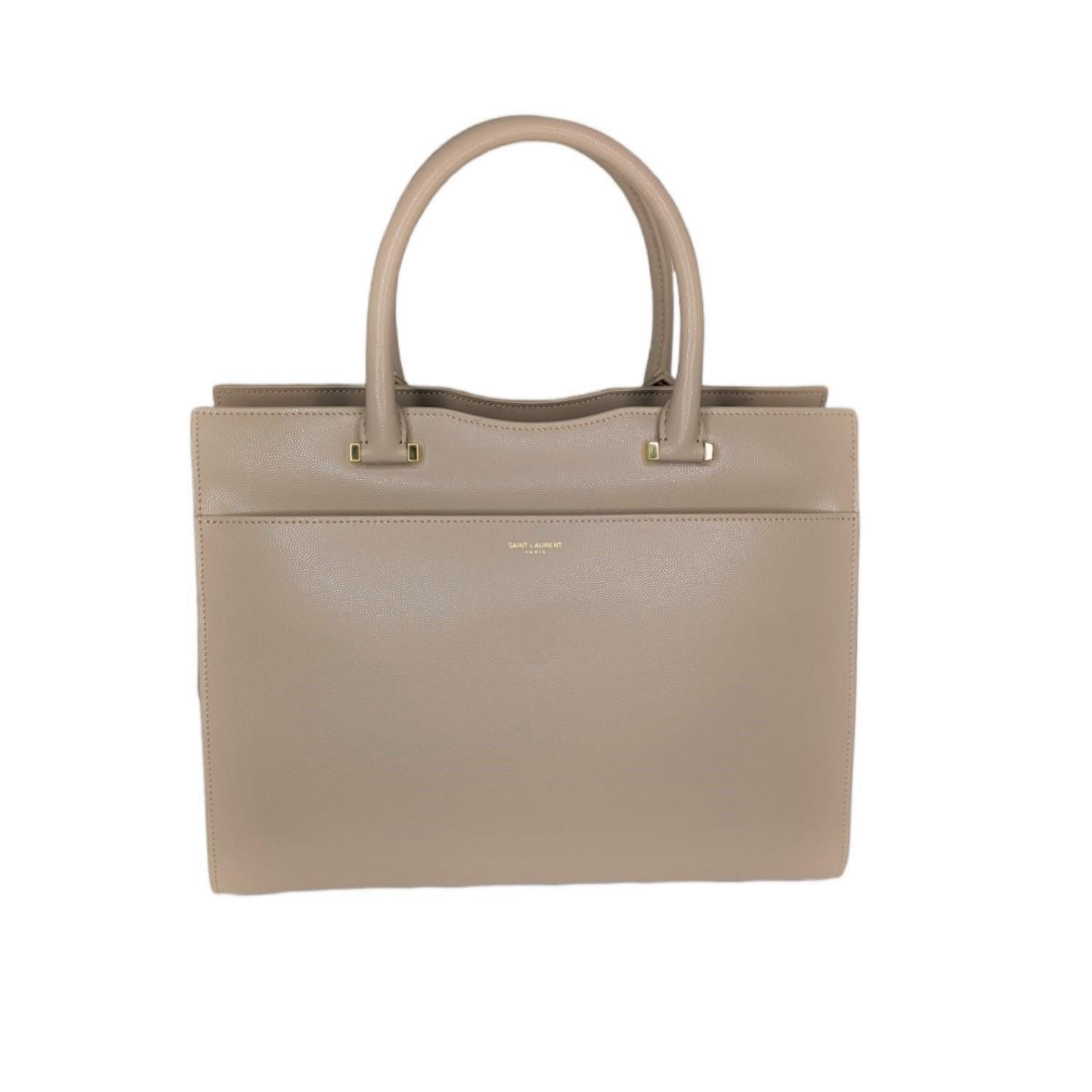 This tote is crafted of smooth calfskin leather in beige. The bag features rolled leather top handles, with polished gold-tone hardware and a front pocket. The top opens to a black partitioned fabric interior with a patch pocket. The bag features a