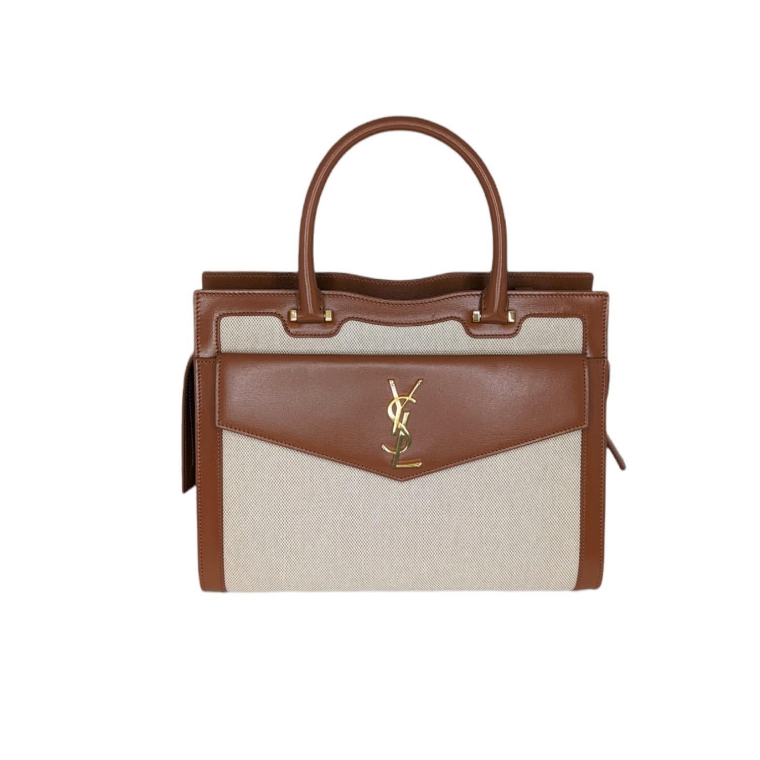 Saint Laurent YSL Medium Uptown Bag in Toile Canvas

Saint Laurent manifests structured elegance in this Uptown Medium tote. Crafted in Italy from cotton canvas with leather trim and luminous golden hardware, this bag features a coordinating clutch