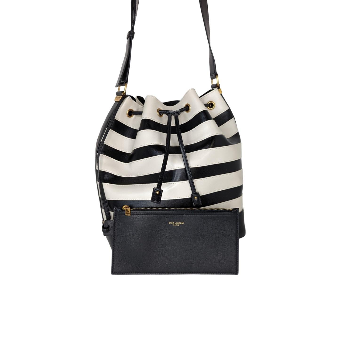 This Saint Laurent black and white stripe tote is crafted of smooth calfskin leather. This bag features a black leather drawstring closure and black top strap with gold hardware. The top opens to a spacious leather interior. The softly structured