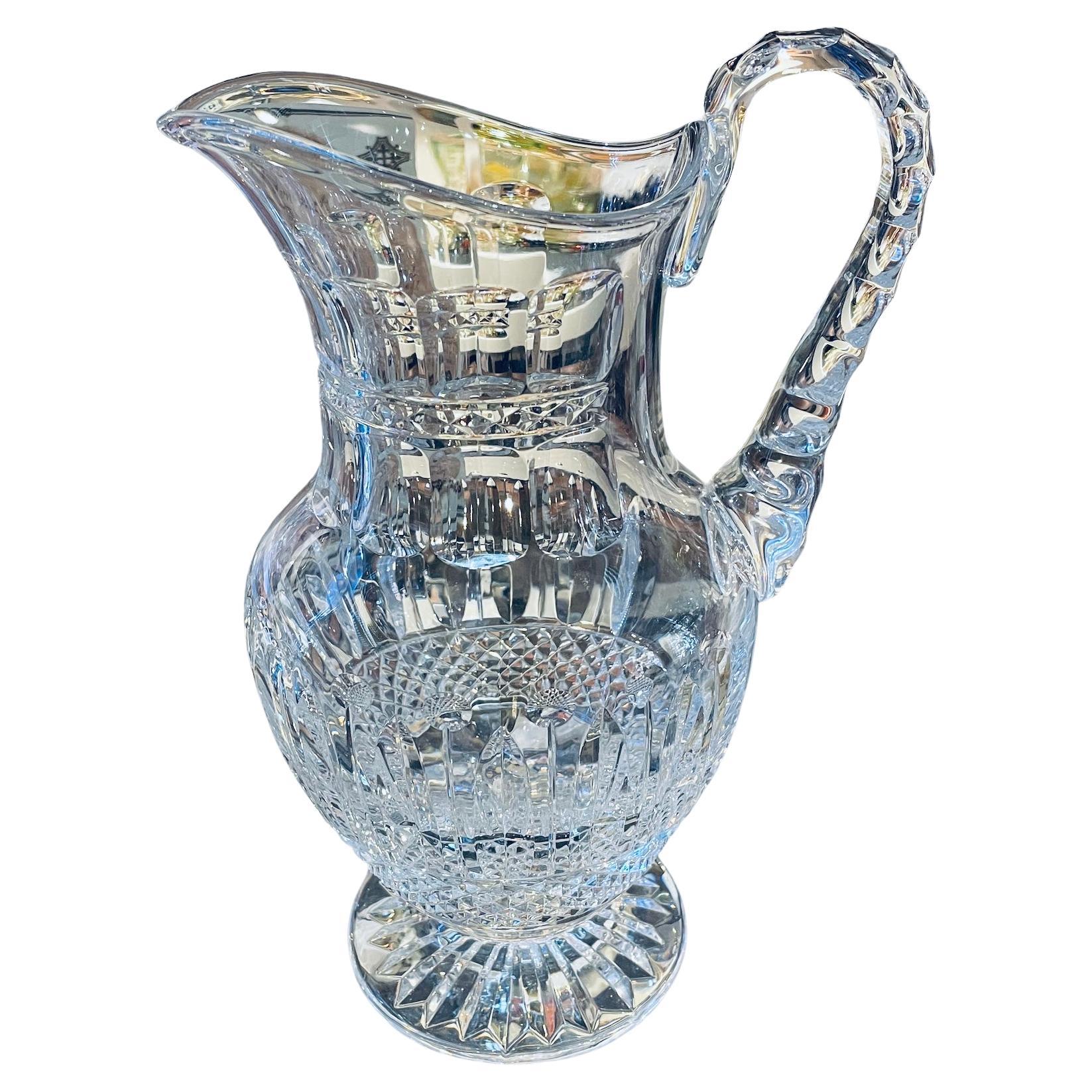 This is a Saint Louis Crystal Tommy pattern Water Jug with handle. It depict a clear crystal adorned with a cluster of diamonds cut pattern at the bottom of the body. Above it, there is a pattern made of feather like cut alternated with sticks with