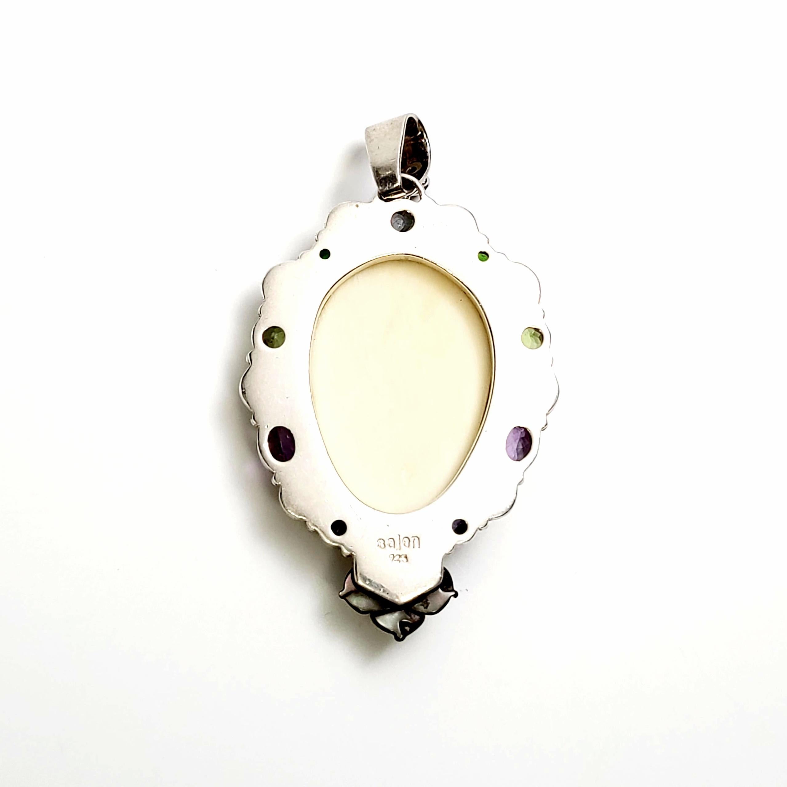 Pendentif en argent sterling Sajen avec visage de déesse en coquillage sculpté et plusieurs pierres précieuses.

Ce pendentif unique en argent sterling est serti dans un cadre en forme de tourbillon avec des pierres précieuses multicolores et une