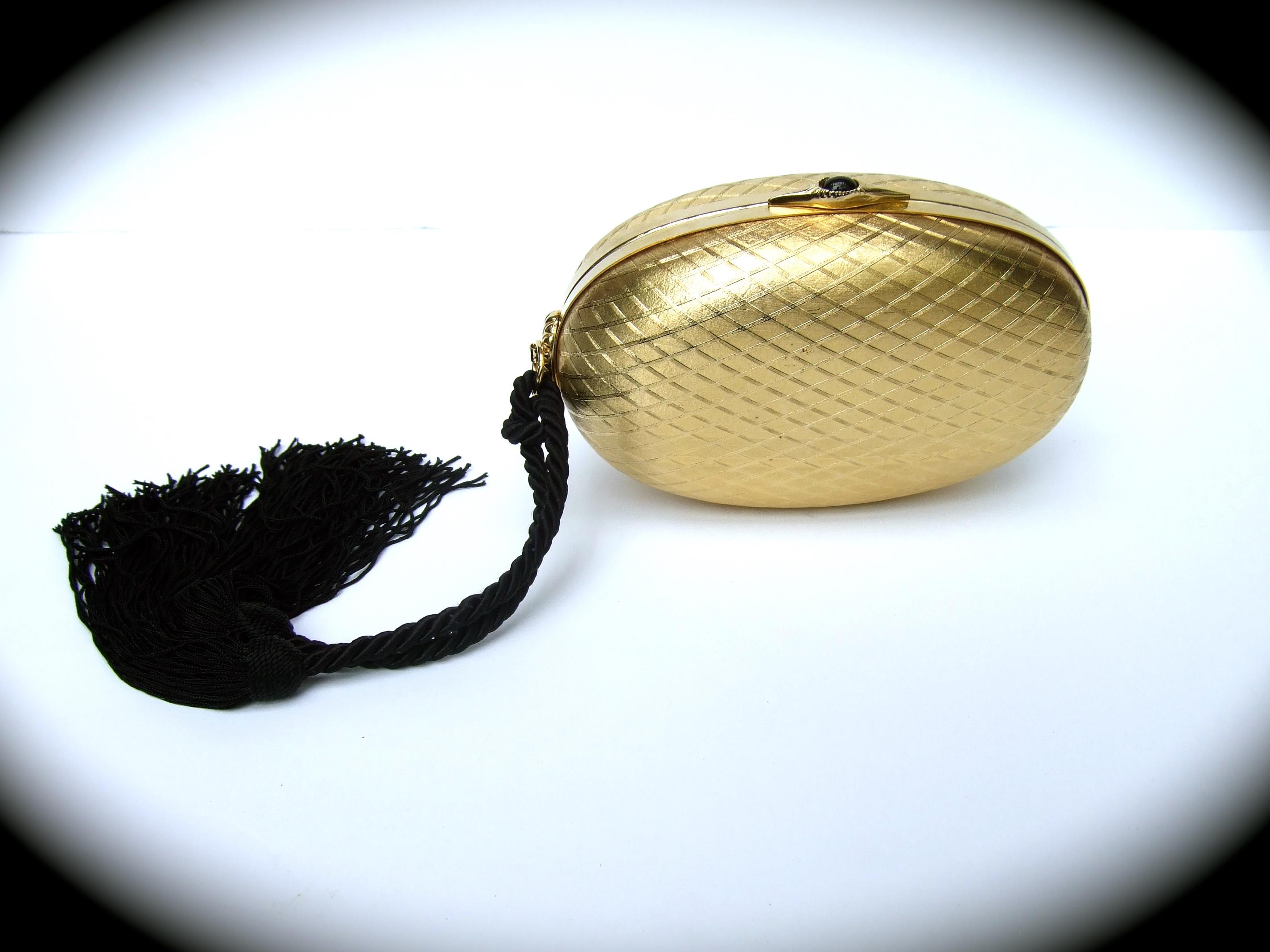 Saks Fifth Avenue Italian gilt metal tassel minaudiere' evening bag c 1970s 
The elegant oval shaped evening bag is designed with a subtle criss cross 
geometric diamond shaped covering 

Adorned with a black fringe rope tassel on one side. The