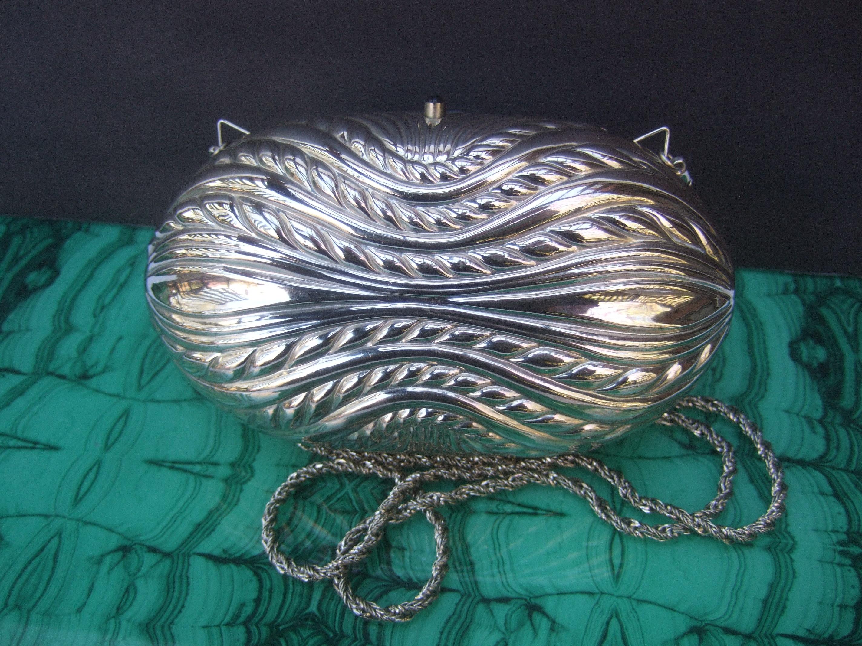 Saks Fifth Avenue Opulent Italian silver metal minaudiere' c 1980s
The elegant oval-shaped silver metal evening bag is embellished with sinuous grooved designs
The versatile evening bag transitions from a chic clutch into a stylish shoulder bag