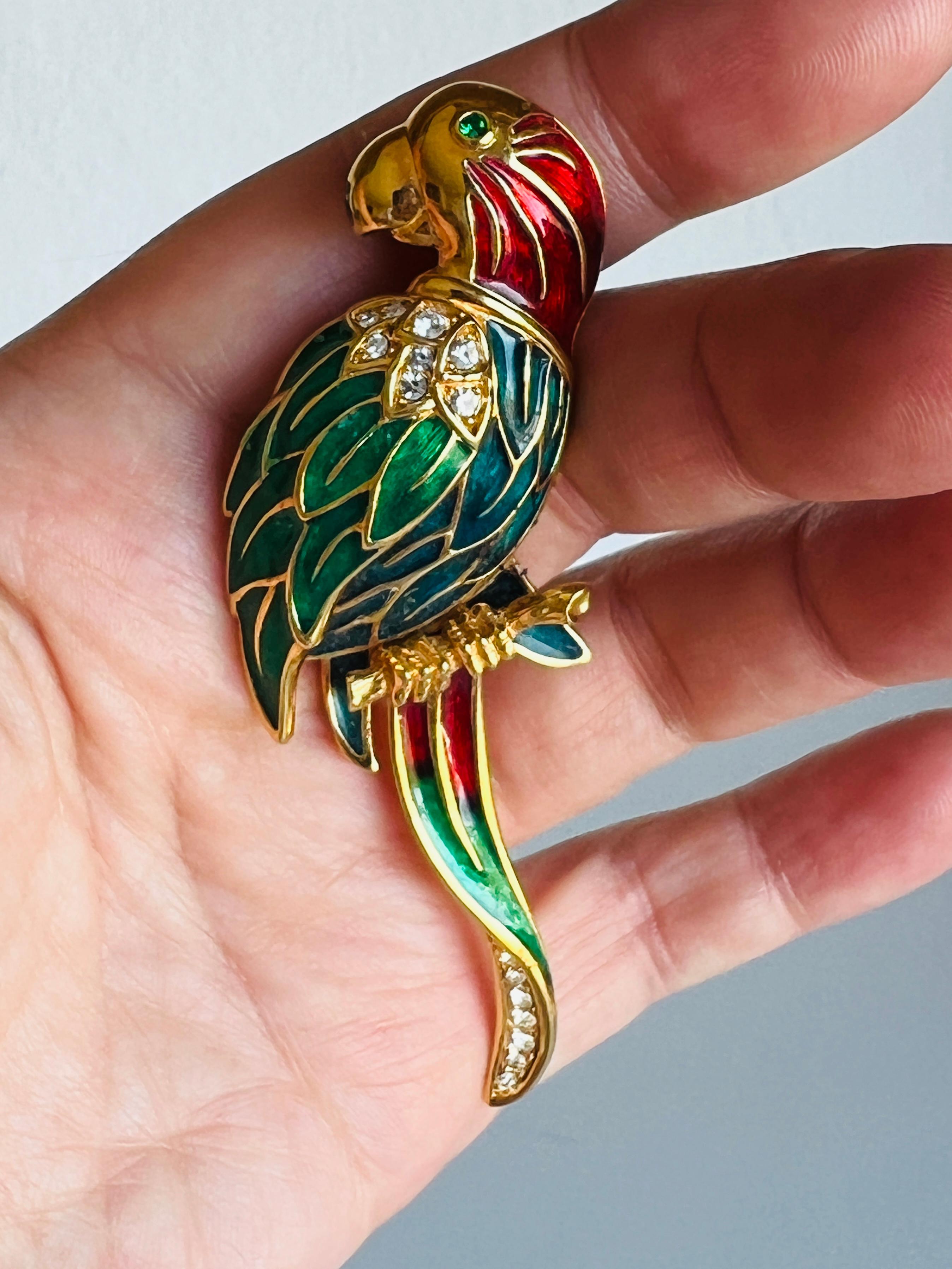 Cette broche perroquet unique et fantaisiste présente un émail vibrant dans des tons rouges, bleus et verts, rehaussé de strass étincelants pour un effet éblouissant. Les détails complexes donnent vie au perroquet, dont l'œil expressif en strass