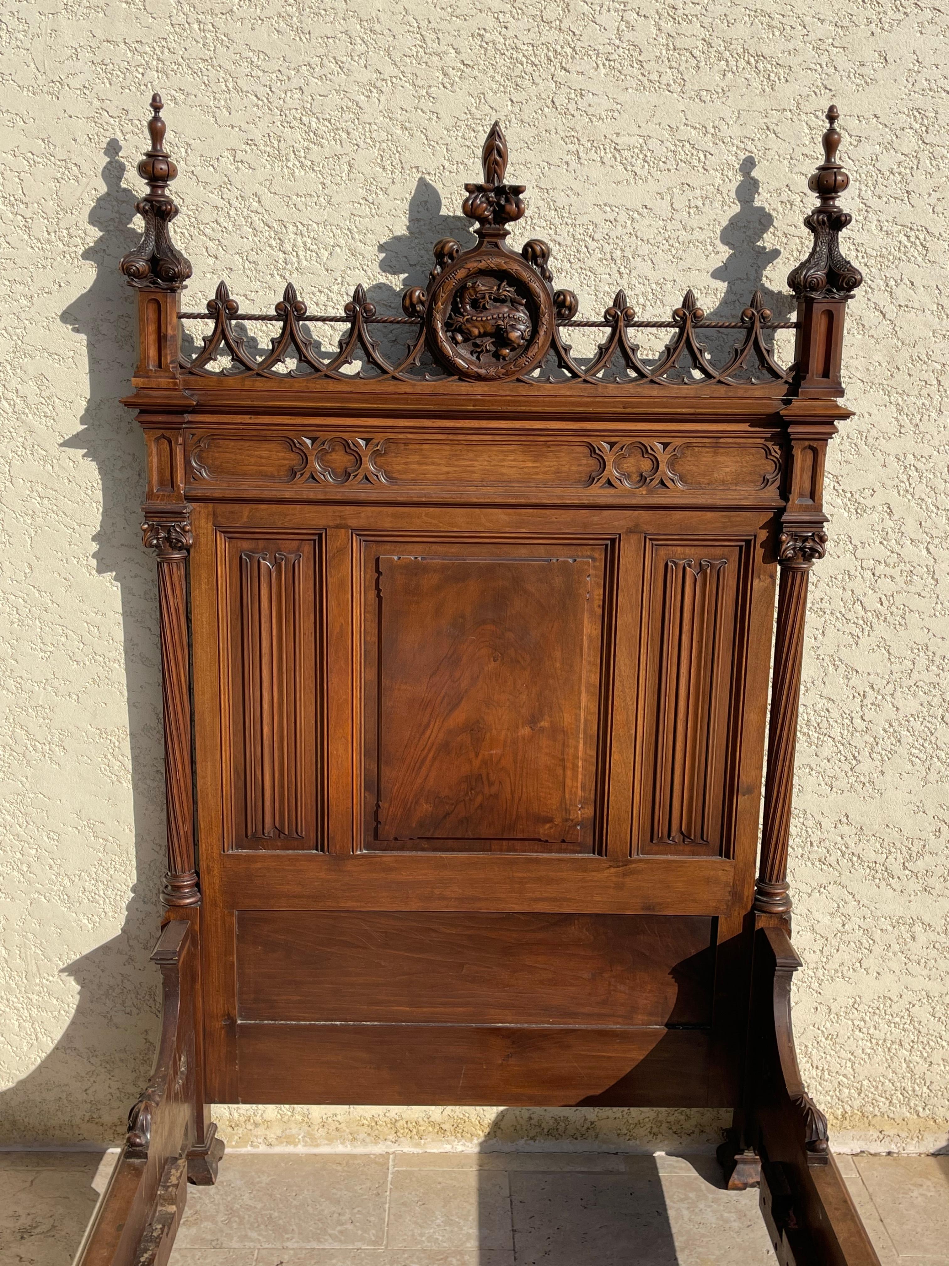 Superb single bed in fully carved walnut in Neo-Gothic style. Pediment decorated with a salamander in the heart of a macaron with points on either side with fish bodies. It is in very good condition. It can also be combined with another neo-Gothic