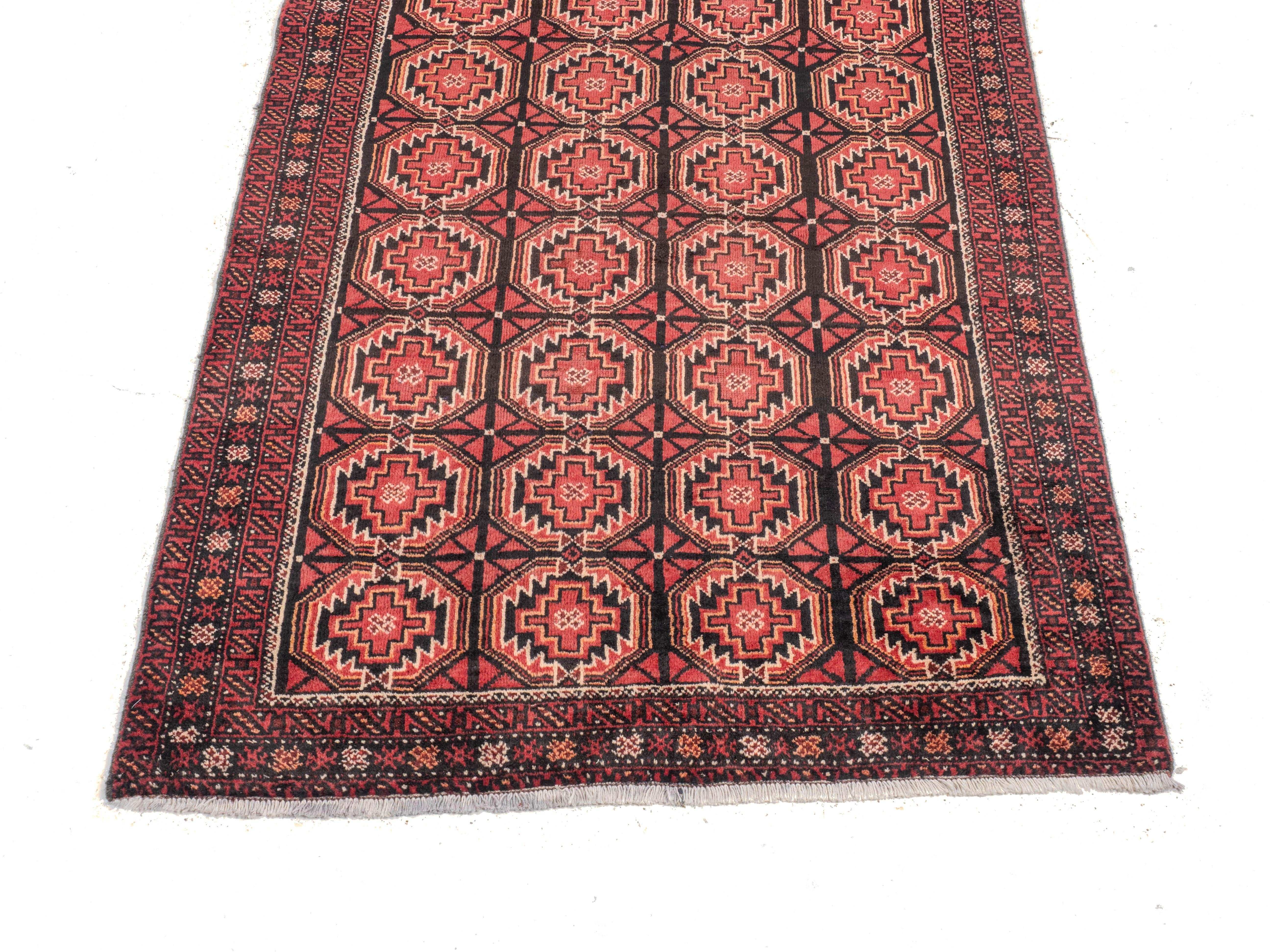 Un tappeto Baluch della regione di Khorasan (Afgano/Persiano), di circa 1 metro e 60 x 1 metro e 80, risalente alla metà del XX secolo. Il campo di colore rosso con colonne di Guls Guls seghettate, racchiuse da bordi stretti a tripla ripetizione. Un