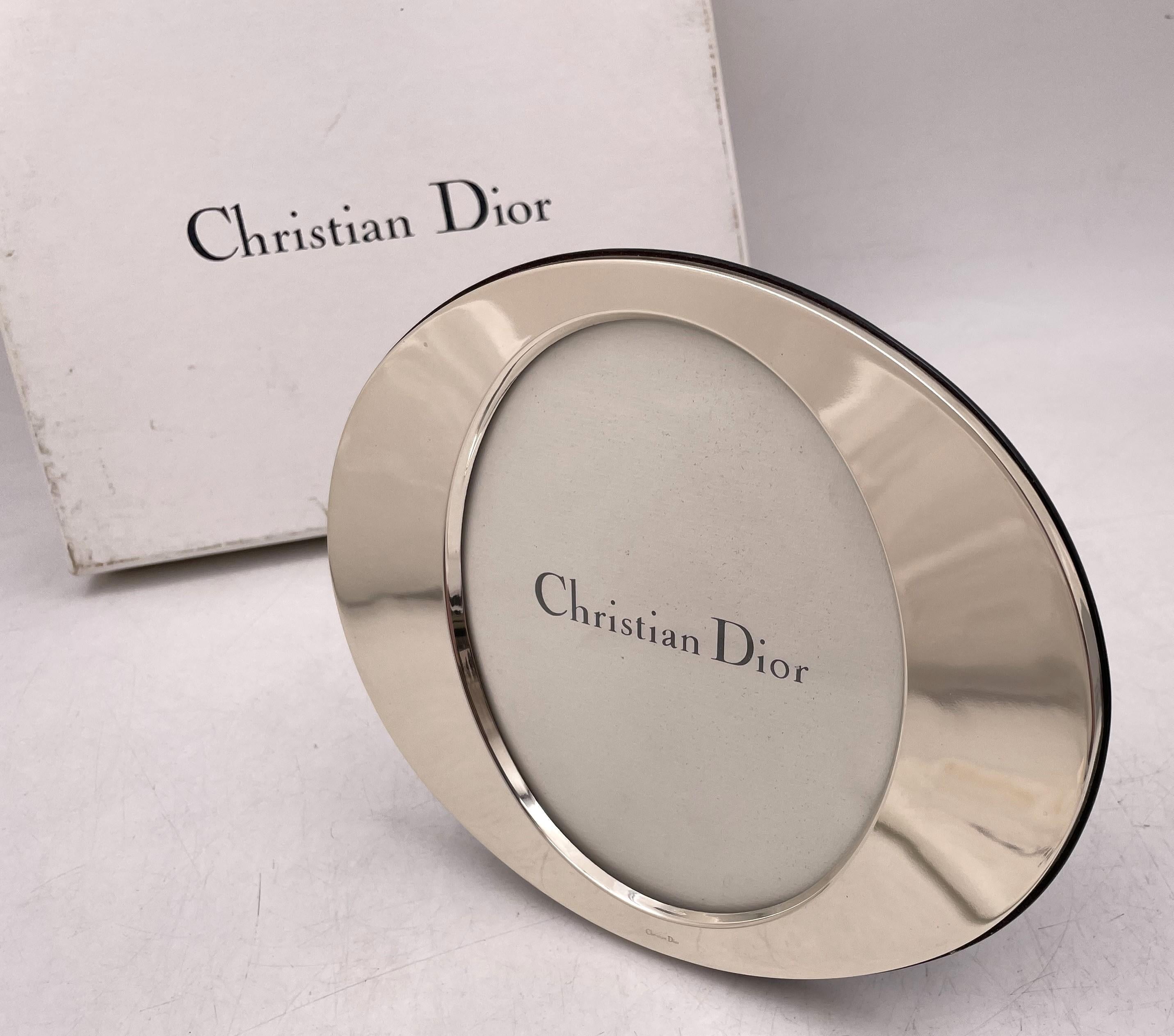 Christian Dior sterling silver picture frame in Mid-Century Modern style, made in Italy, and in oval shape. In new condition and sold with its original papers, pouch, and box, it has a wooden back, measures 8 1/4'' by 6 5/8'' (inner dimensions are 5