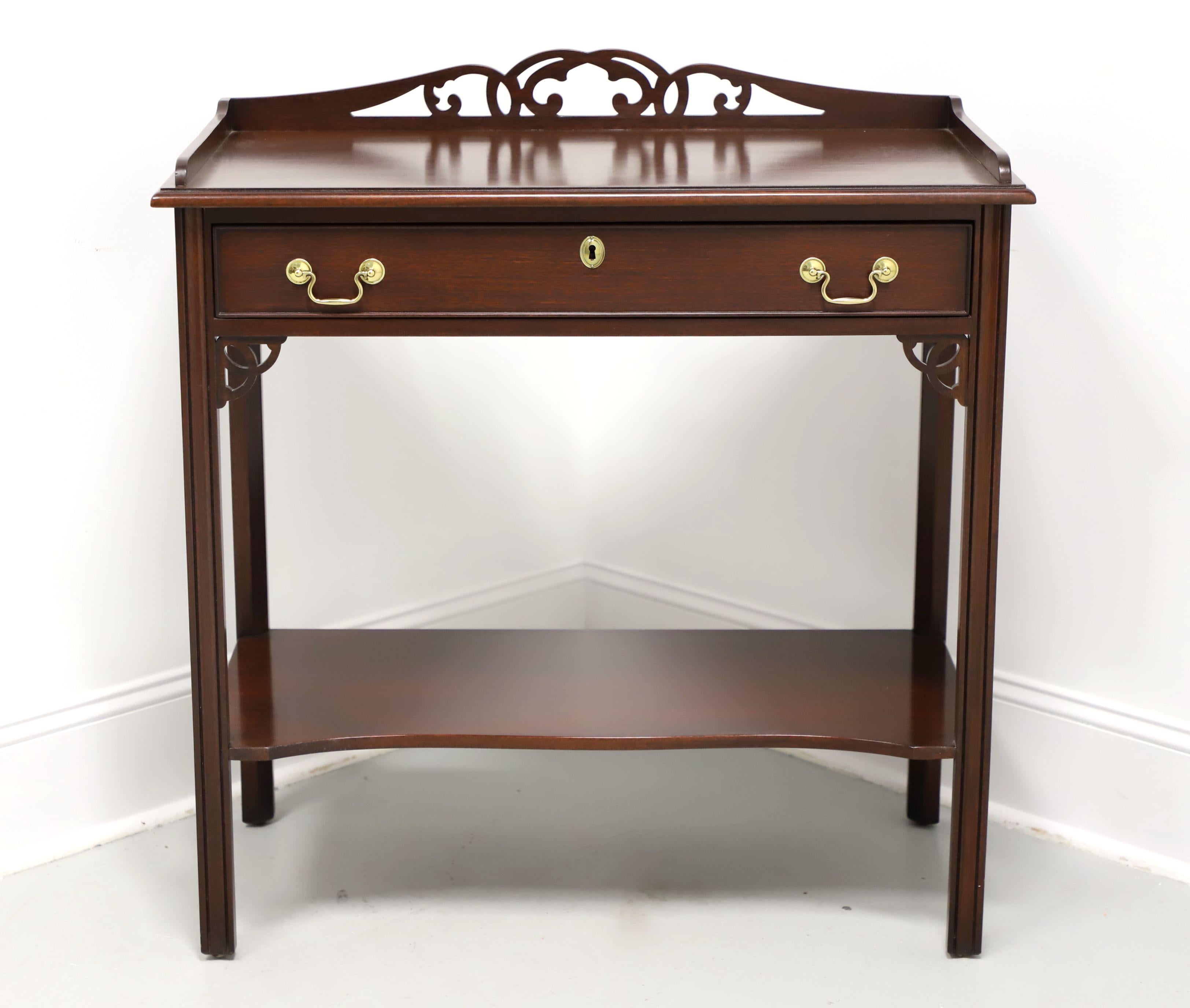 A Chippendale style console table by Salem Square. Mahogany with brass hardware, carved fretwork gallery to bevel edge top, decorative fretwork accents at leg joints, an undertier shelf, and fluted straight legs. Features one drawer of dovetail