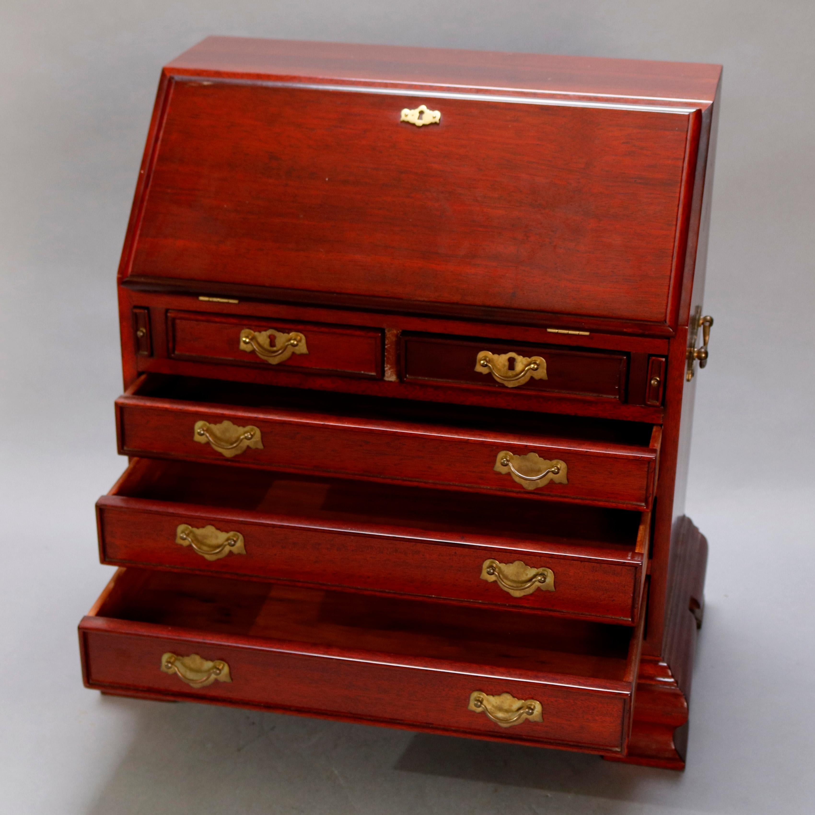 A miniature Chippendale style salesmen's sample tabletop display desk offers diminutive mahogany construction with slant front opening to reveal writing surface and pigeon holes surmounting two smaller drawers over three long drawers and seated on