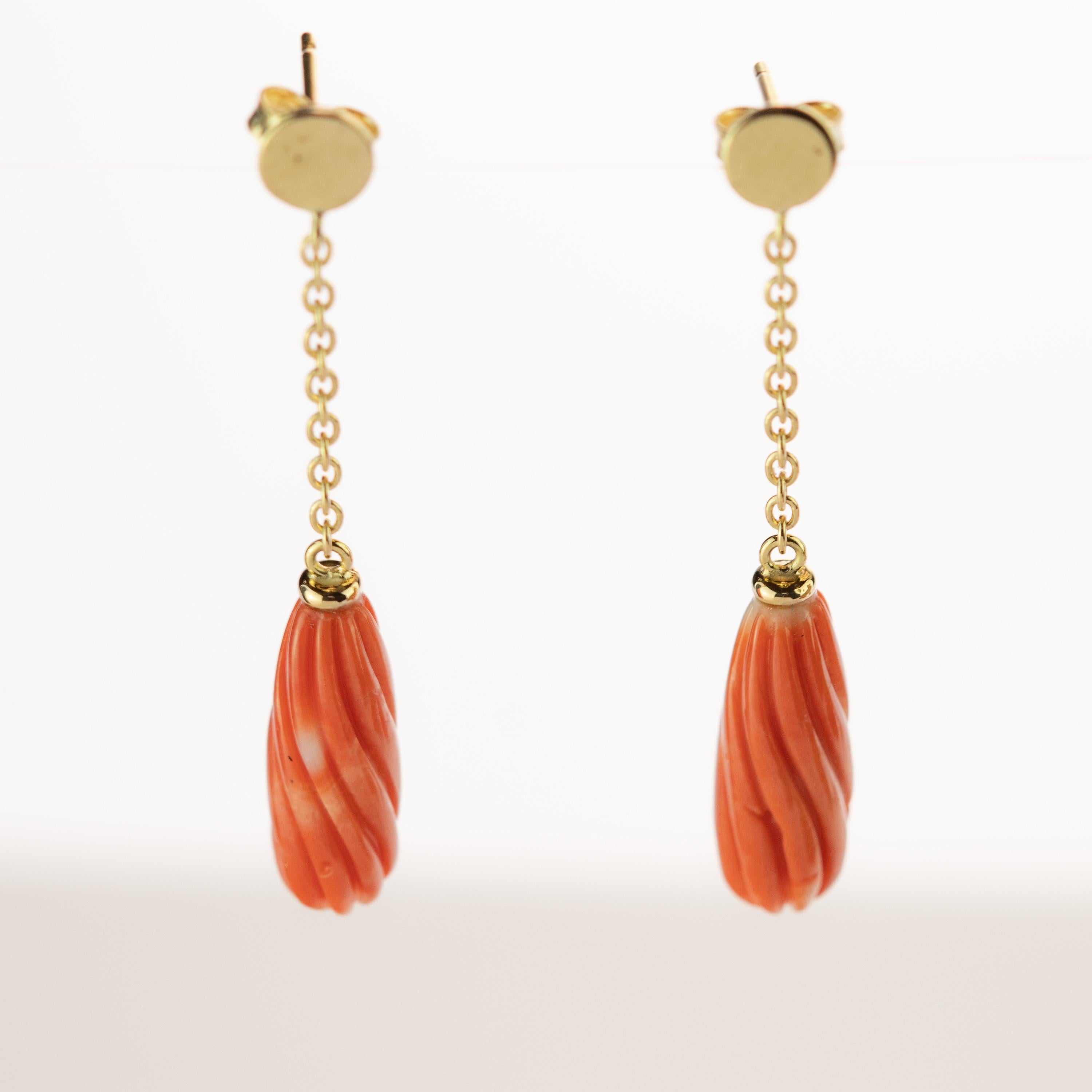 Exotic earrings design. The 18 karat yellow gold enhances the piece with a round circle that is connected to a delicate chain holding a beautifully carved and light salmon natural coral long shaped gem. Italians own the art of coral carving. For