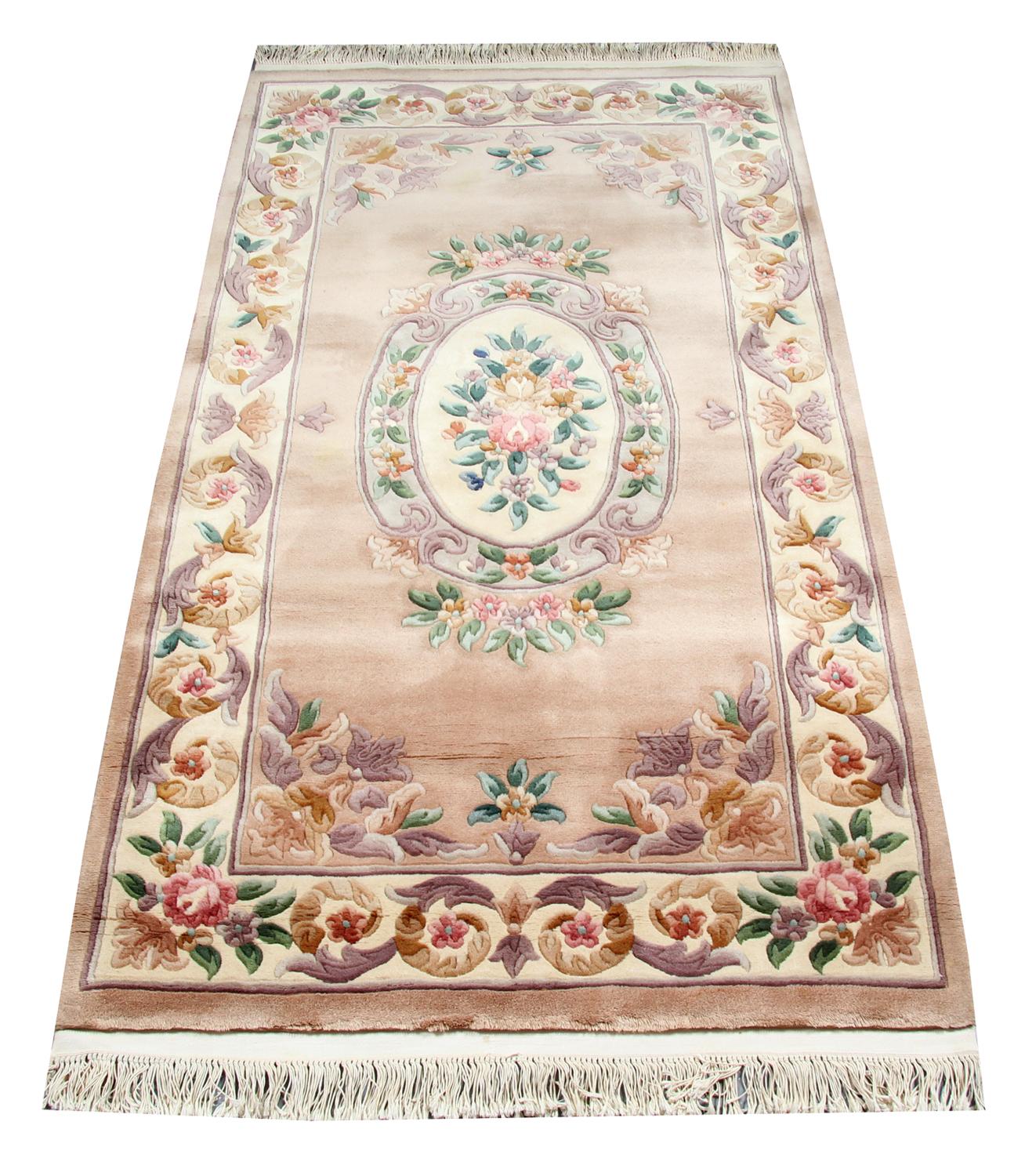This elegant handmade carpet was constructed in the 1960s in China. The central design has been woven on a peach/ pink field with orange, purple and green accent colours that make up the floral medallion and the symmetrical surrounding design. This