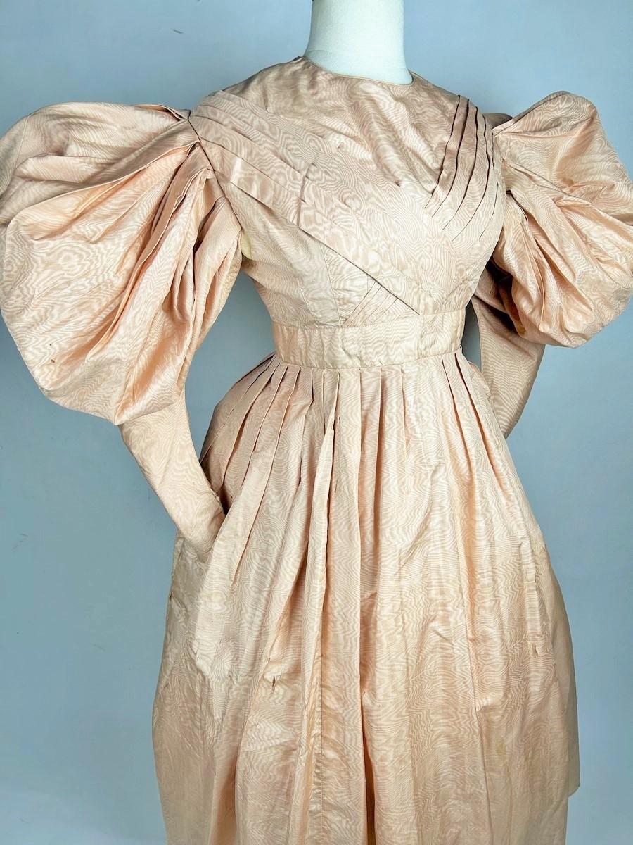 CIRCA 1830 -1835
Frankreich Louis-Philippe-Periode
Lachsrosa Seidenmoiré-Dinner-Kleid mit weiten, über die Unterarme gezogenen Gigot-Ärmeln aus der extravagantesten Periode der Romantik. Das Mieder ist am Hals tailliert und wird am Rücken mit