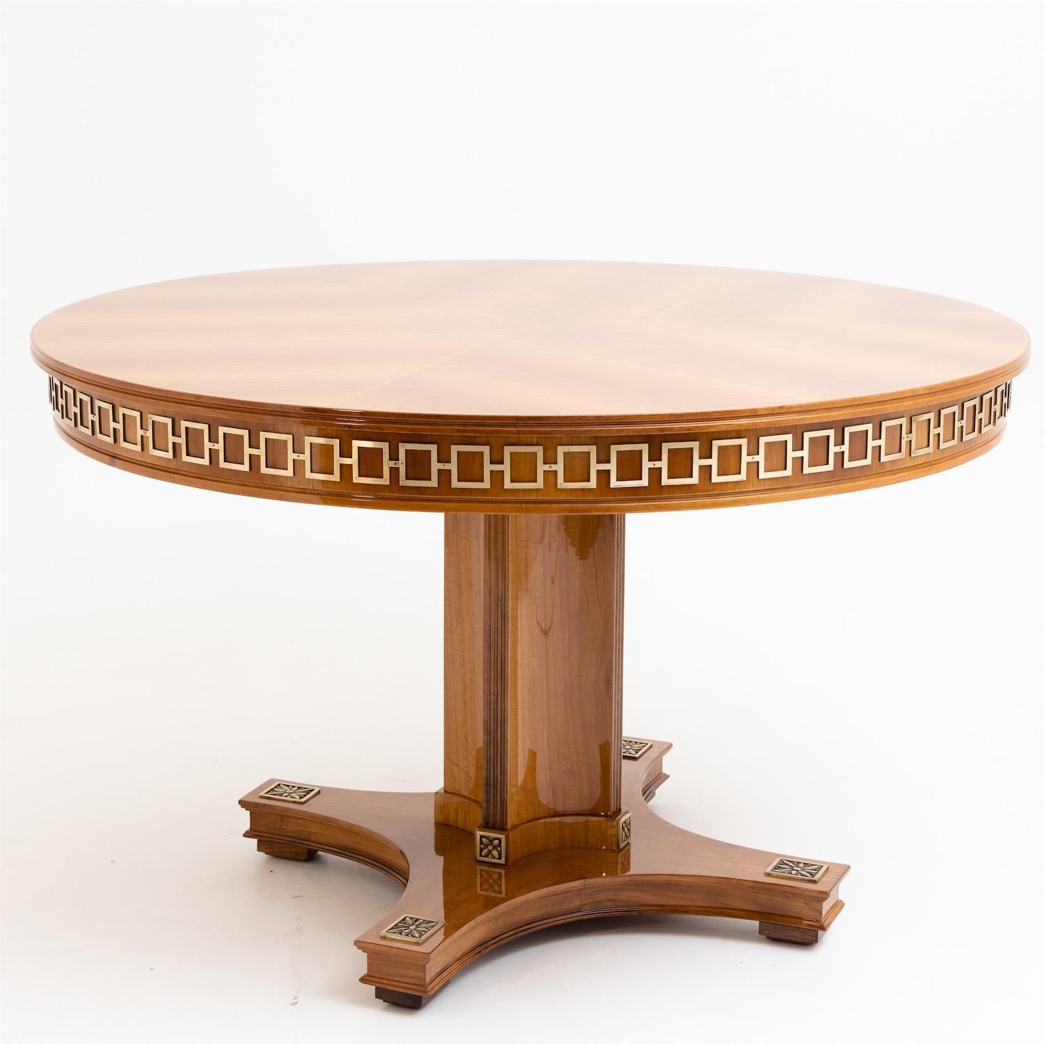 Salon table standing on a quatrefoil stand with a round tabletop and a geometric brass band on the frame. The foot is decorated with plaques with flower motifs; the tabletop is inlaid with fine stylized acanthus leaf motifs. The table has been