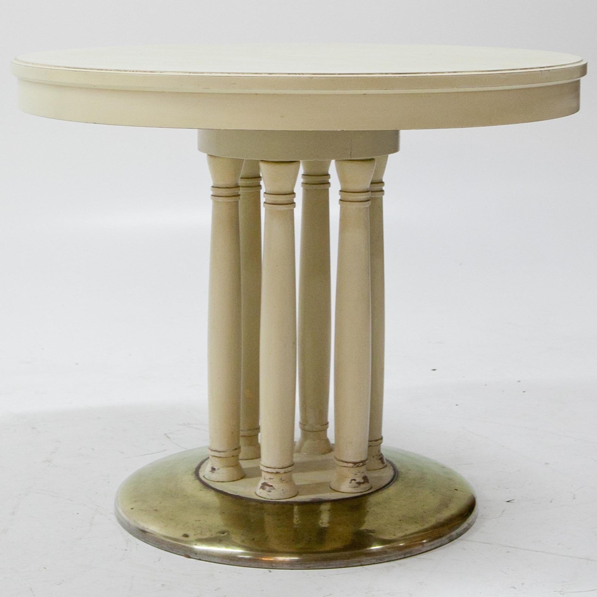 Round crème-white salon table of the Viennese Secession, standing on a round brass foot. Six columns support the tabletop. The table shows signs of age and use.