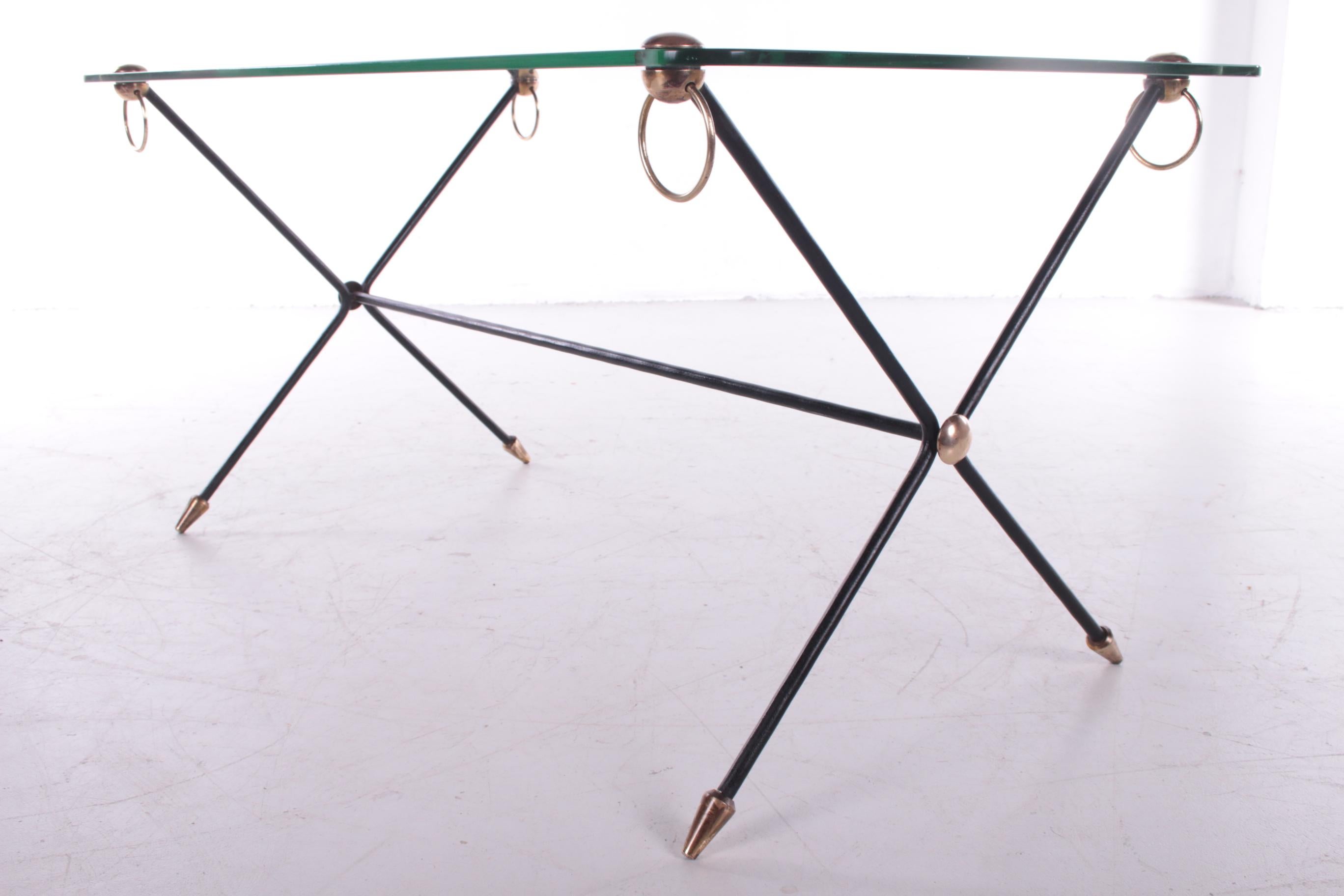 A beautiful coffee table with black metal legs.
The design is also called an X model because of the shape of the legs.
This is a design by the French designer Jacques Adnet, made around the 1960s.

The bottom of the legs are finished with bronze