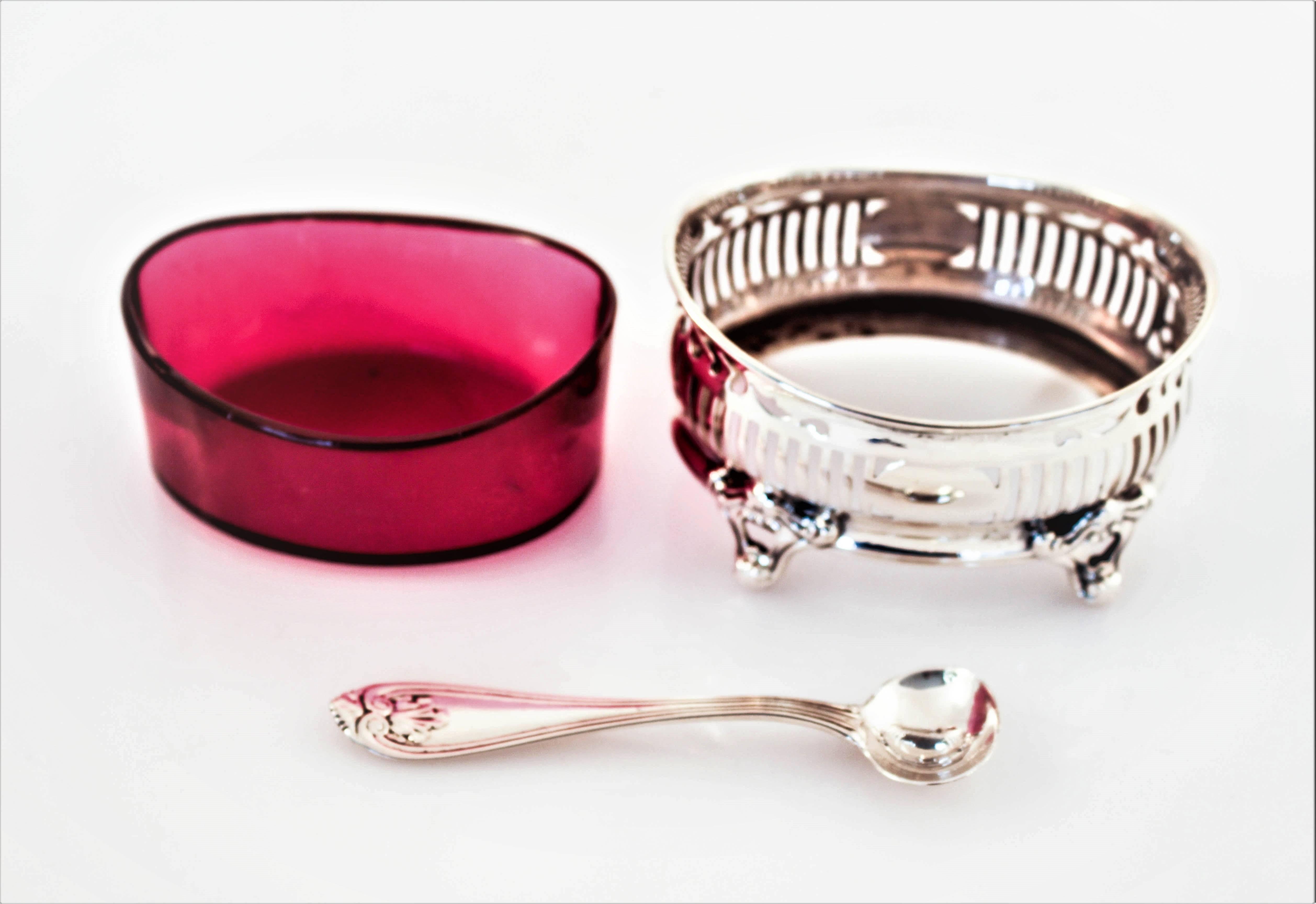 From beneath the silver a burst of cranberry-red glass pops out, it brings life to this piece. Oval in shape, this salt cellar sits on four legs, thereby raising it off the surface. The original silver spoon sits inside. The glass insert comes out,