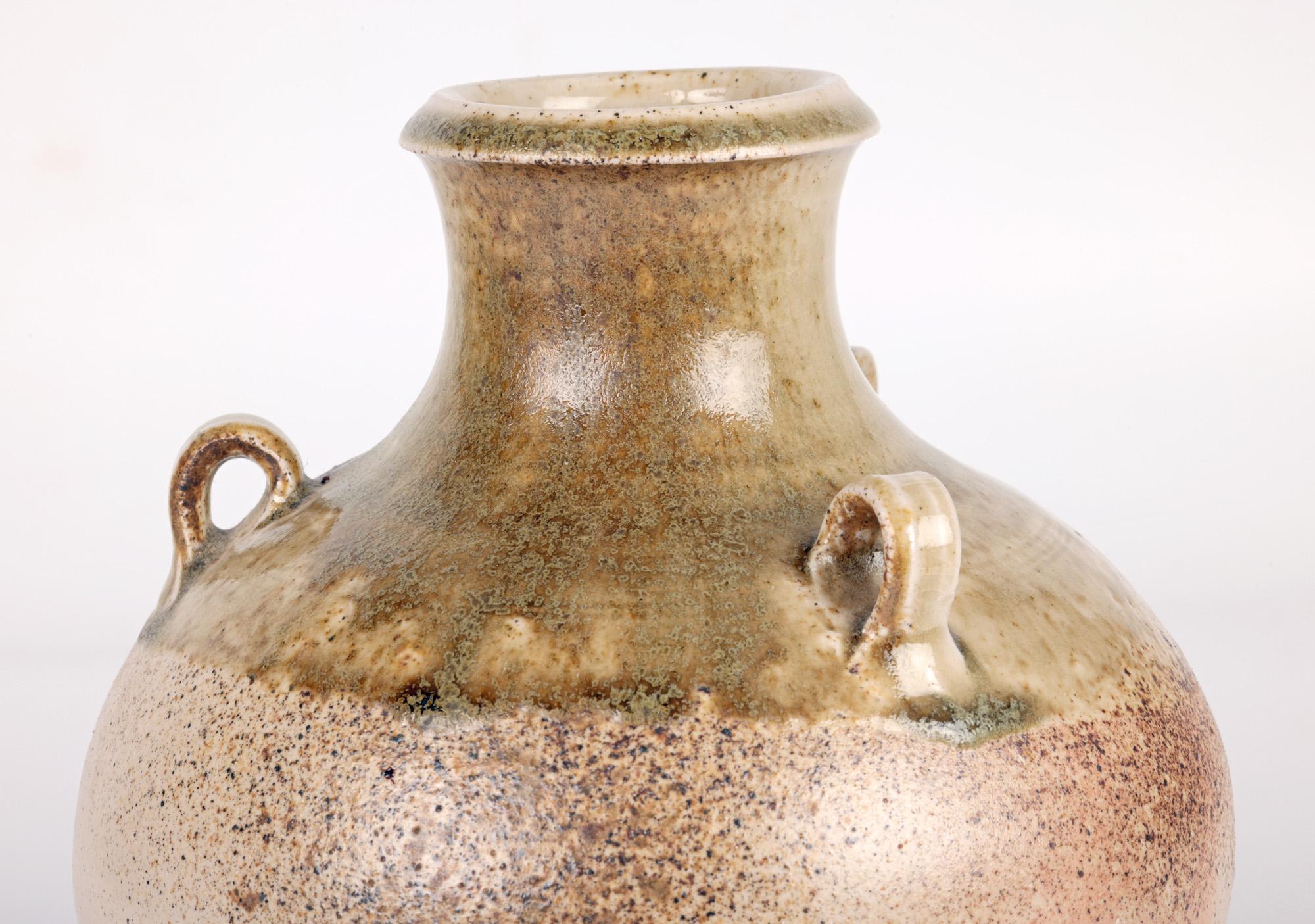 A very stylish British studio pottery three handled bottle vase decorated in salt glazes signed to the base and dating from the 20th century. The hand thrown vase stands on a narrow round base with a finely combed finish with a round bulbous shaped