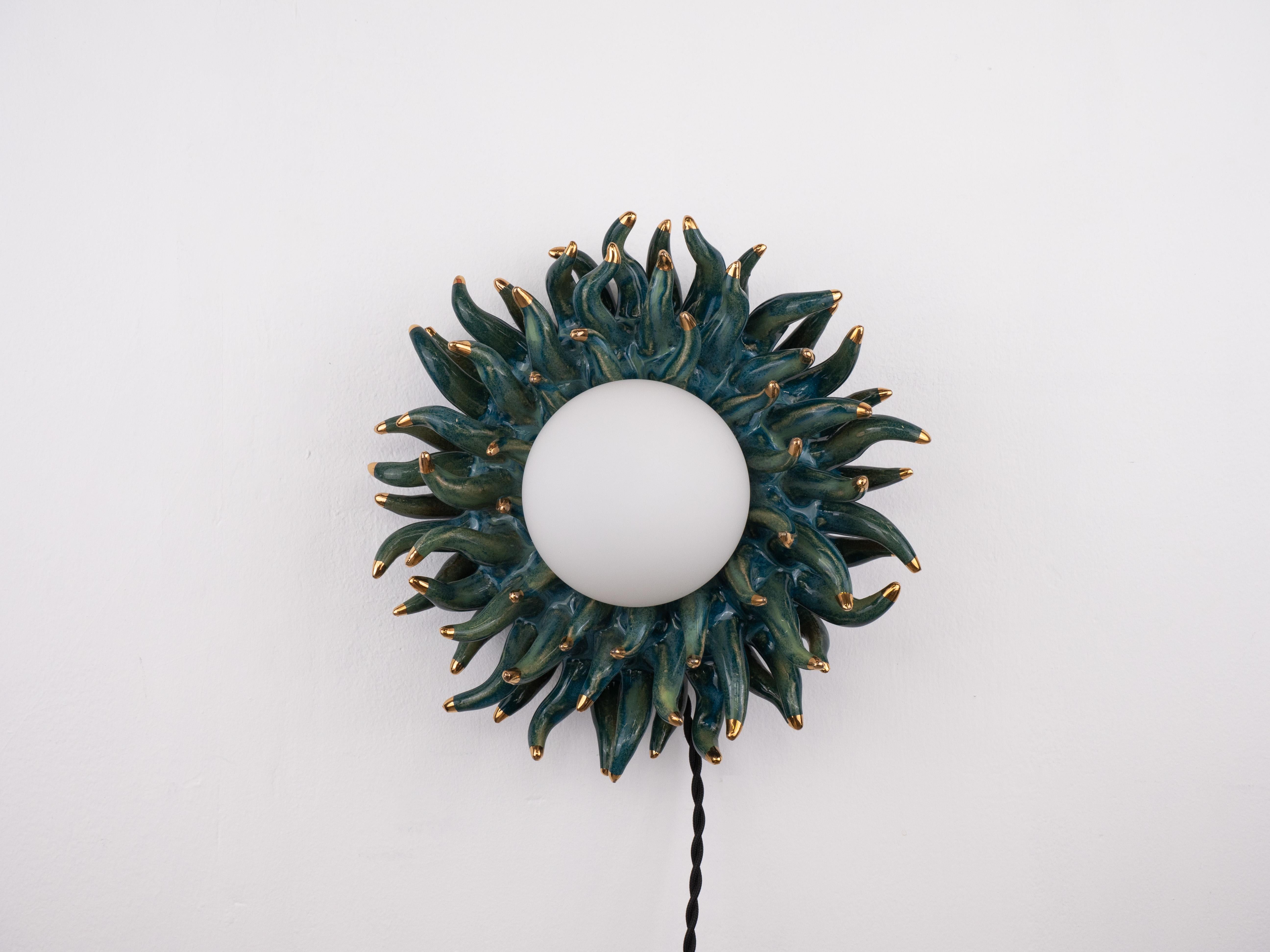 Este cautivador aplique de pared tiene un diseño tentacular que parece bailar con energía. Con tonos verdes y azules, puntas de oro de 24 quilates y un acabado brillante, irradia un brillo de otro mundo. 

Bombilla incluida
Portalámparas: