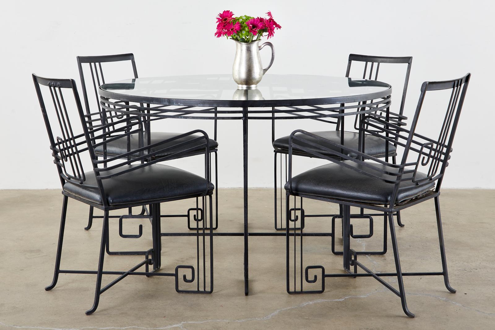 Unique wrought iron garden dining table and chairs crafted in the Art Deco taste. The set features a neoclassical Greek key motif reminiscent of John Salterini's Mid-Century Modern designs. The sculptural style showcases the thin line iron frames