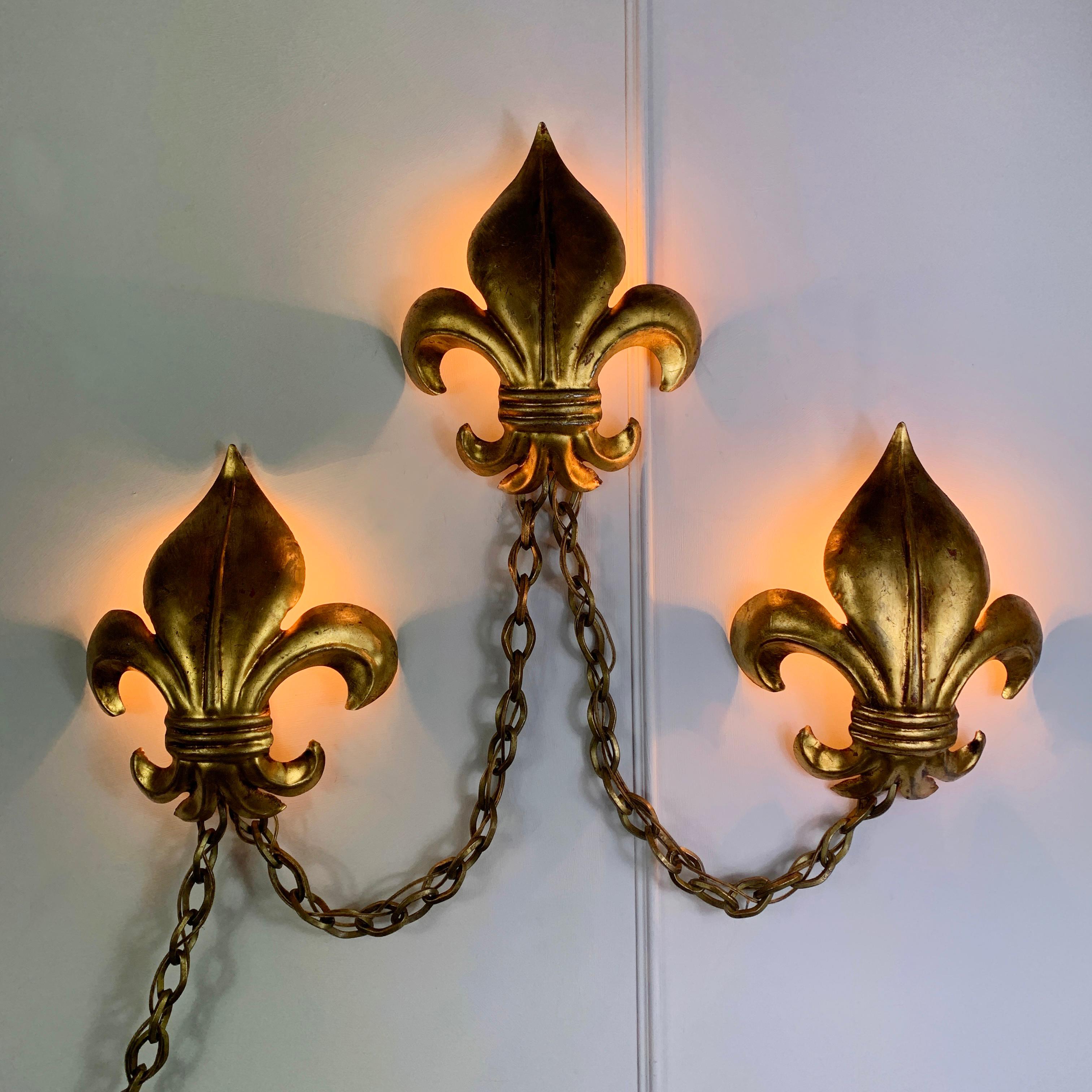 A stunning Salvadori 1970's Italian trio of Fleur de Lis chained wall lights. Each of the Fleur de Lis house a single bulb holder to the rear, and are joined to each other with a length of heavy gilt iron chain. 

Each Fleur de Lis 29cm height,