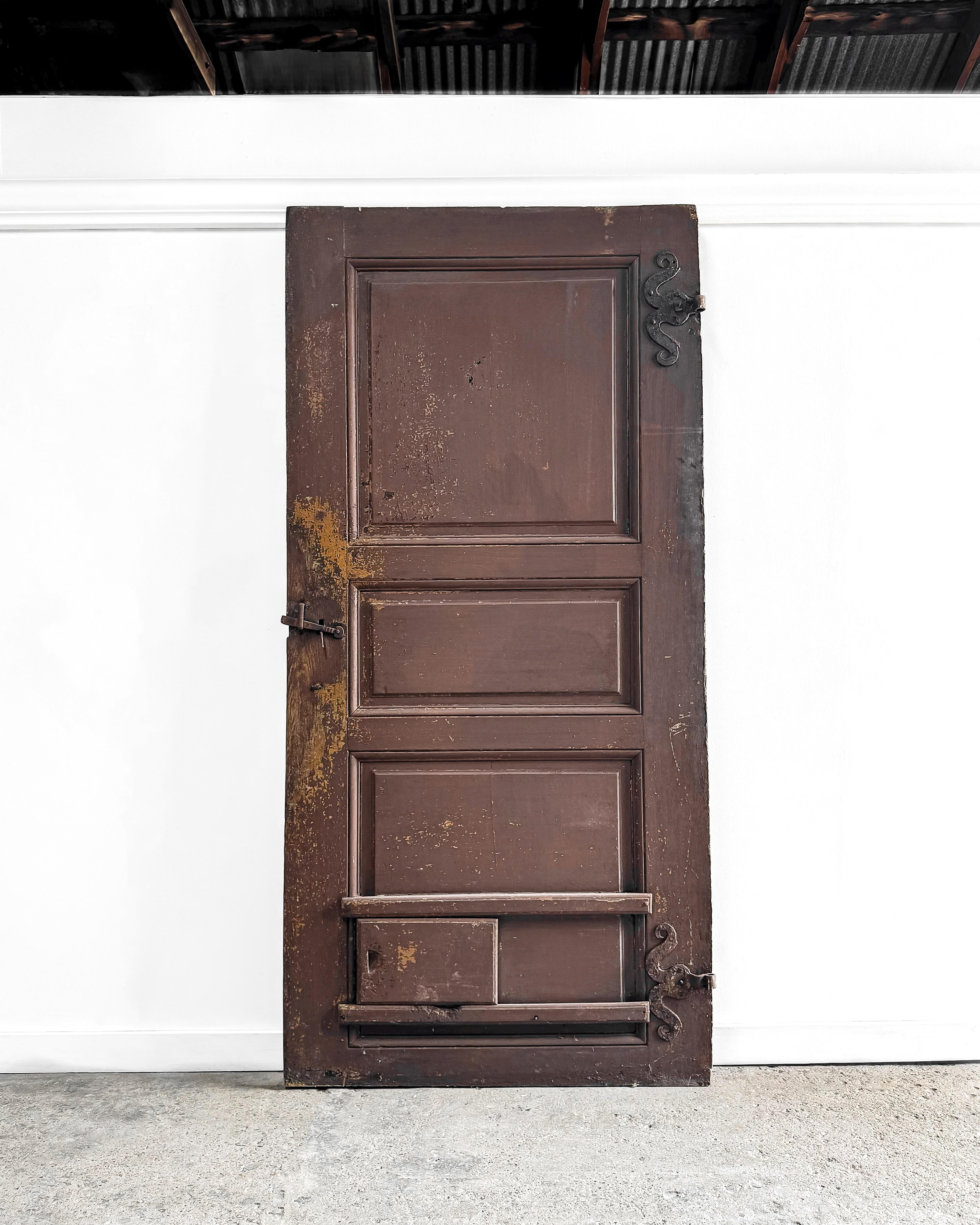 A reclaimed French door with a raised 3-panel configuration and grooved molding detailing, perfect for incorporating into any modern home. The door features beautiful iron hardware and a quirky sliding cat door, adding unique character. Its lovely