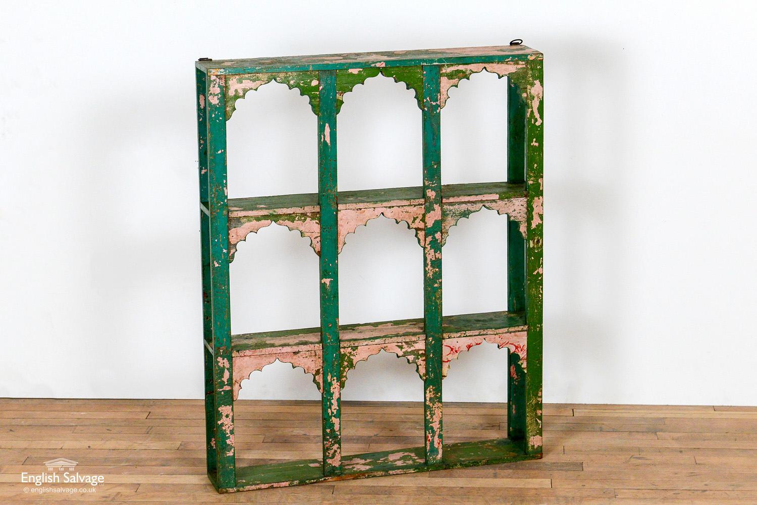 Striking reclaimed wooden shelving or display unit. A beautiful patina has formed from the green paint flaking away to reveal remnants of pink and red paint beneath. Mihrab style inserts arches top each of the nine compartments. Hanging hooks are