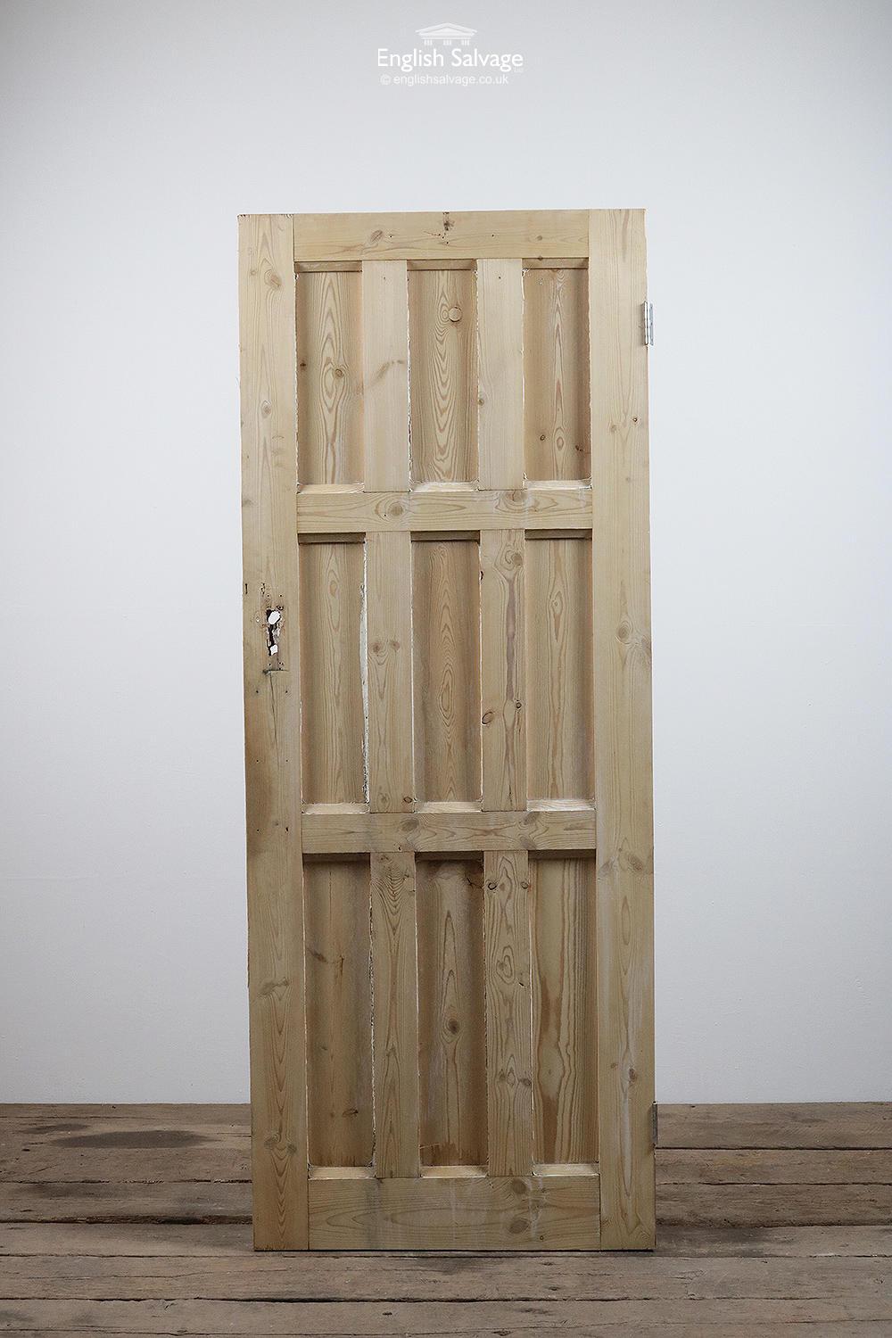 Salvaged stripped pine door with three over three, over three vertical panels and two hinges. Splits to stiles and rails, the door has been cut on a slant and there are lock, handle and nail holes.