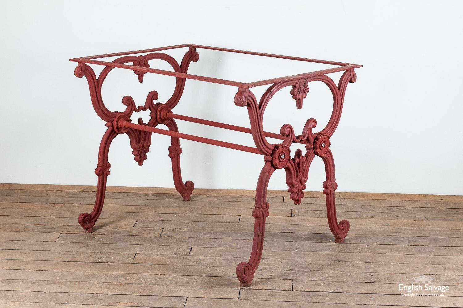Salvaged cast iron table base with ornate floral and foliate detailing. The table appears to painted in red oxide paint. There are two support rails below the table top. This would look amazing with a marble, granite or wood top.