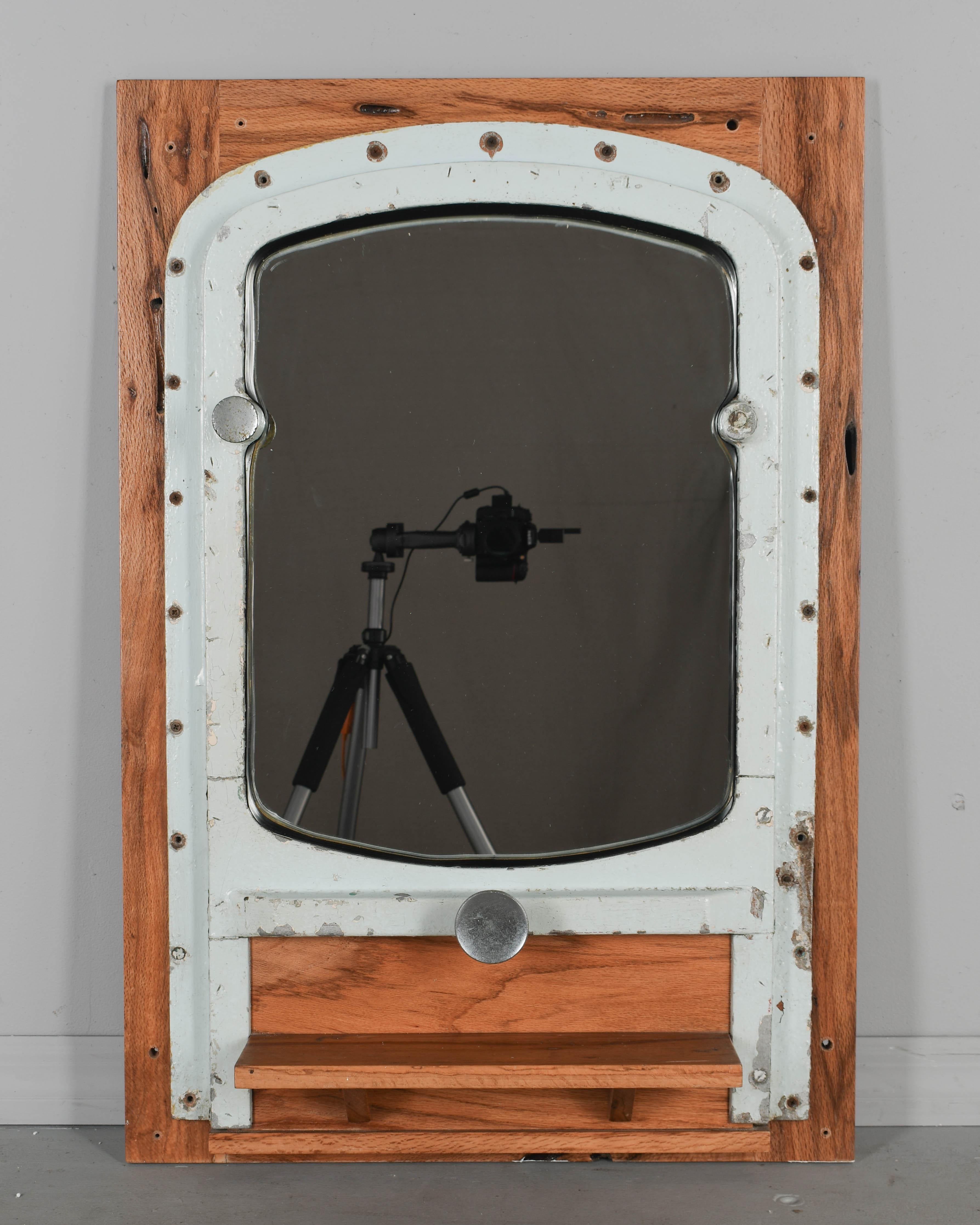 A rustic salvaged ship's portal repurposed into a wall mirror. Mounted to an oak frame with a small ledge or shelf. Pale gray painted steel with minor loses. White glove delivery only because of heavy weight. 
Dimensions: 25.5