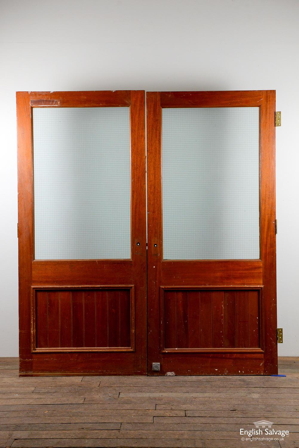 Double teak doors, each with a large intact glazed panel, which could be used as a double or adapted to use as two singles. Each door has three hinges, a few dings, handle, lock and nail holes present.