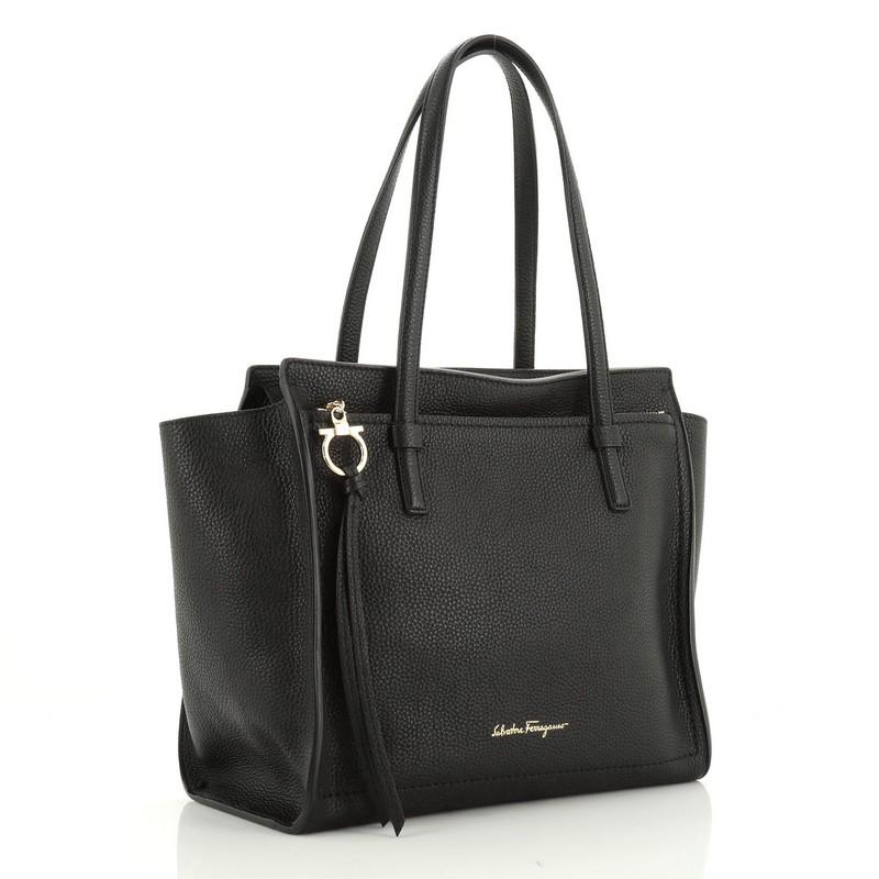 This Salvatore Ferragamo Amy Tote Pebbled Leather Medium, crafted from black pebbled leather, features flat shoulder straps, exterior front zip pocket with Gancio charm zip pull, protective base studs and gold-tone hardware. Its zip closure opens to