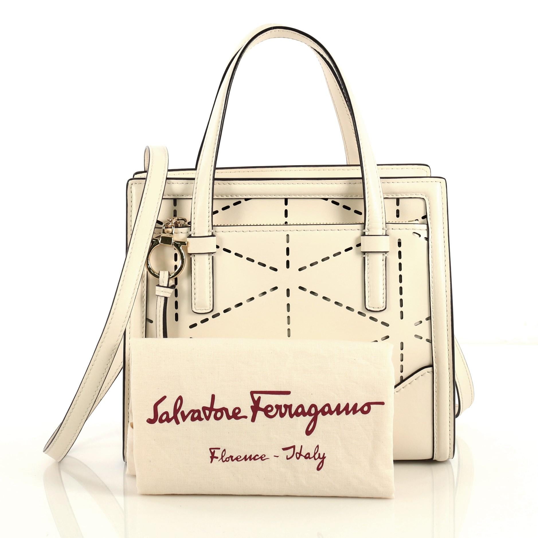 This Salvatore Ferragamo Amy Tote Perforated Leather Mini, crafted from white perforated leather, features dual flat handles, exterior front zip pocket with Gancio charm zip pull, and gold-tone hardware. Its zip closure opens to a brown leather