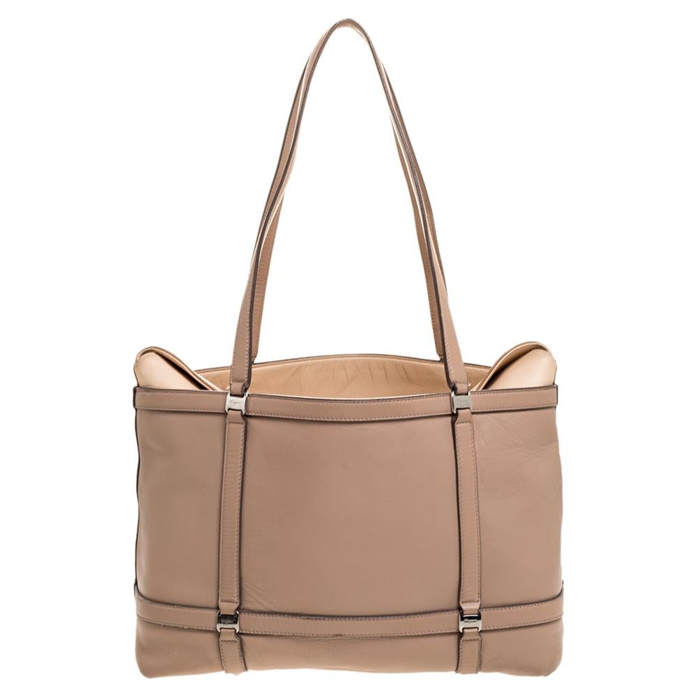 This lovely tote bag is a creation that you cannot miss out on! Designed by Salvatore Ferragamo in Italy, it is crafted from quality leather and comes in a lovely shade of beige. It is held with dual handles, fabric-lined interior, and silver-tone