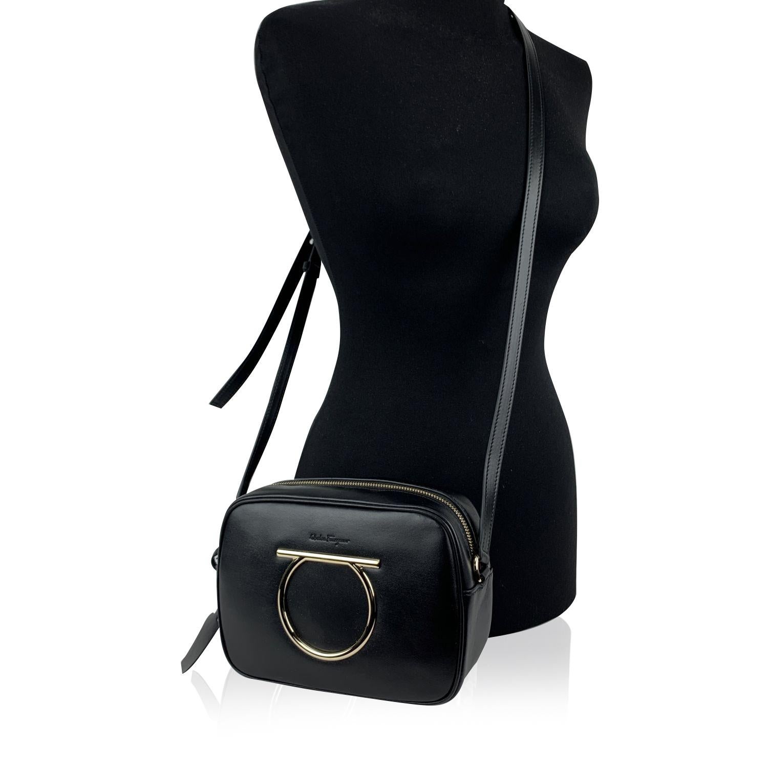 Beautiful 'Vela CC' shoulder bag by Salvatore Ferragamo. Made of black calf leather. It features the Gancino logo detailing on the front in gold metal. Upper zipper closure. Adjustable leather shoulder strap. Canvas lining. 2 side open pockets