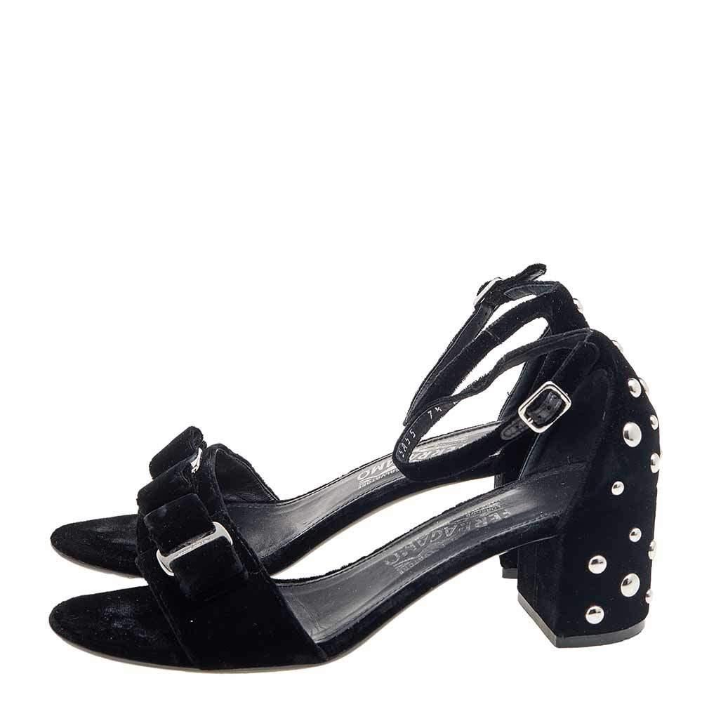 Derrocha clase y perfección al caminar con estas sandalias de Salvatore Ferragamo. Se fabrican con terciopelo negro. Llevan puntera abierta, correa en el tobillo y tacones en bloque con tachuelas. Los herrajes plateados adornan su silueta. ¡Luce un