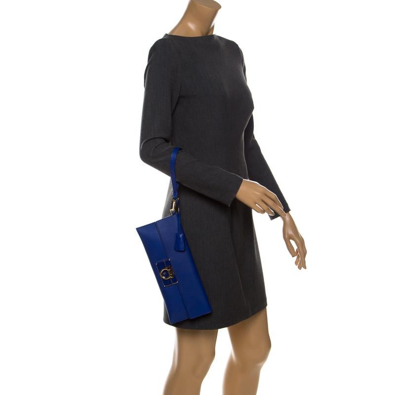Finely crafted from leather, and shining with beauty is this beautiful Afef clutch by Salvatore Ferragamo. It is designed in a blue shade and features their signature Gancio motif detailed on the front flap in gold-tone. Complete with leather