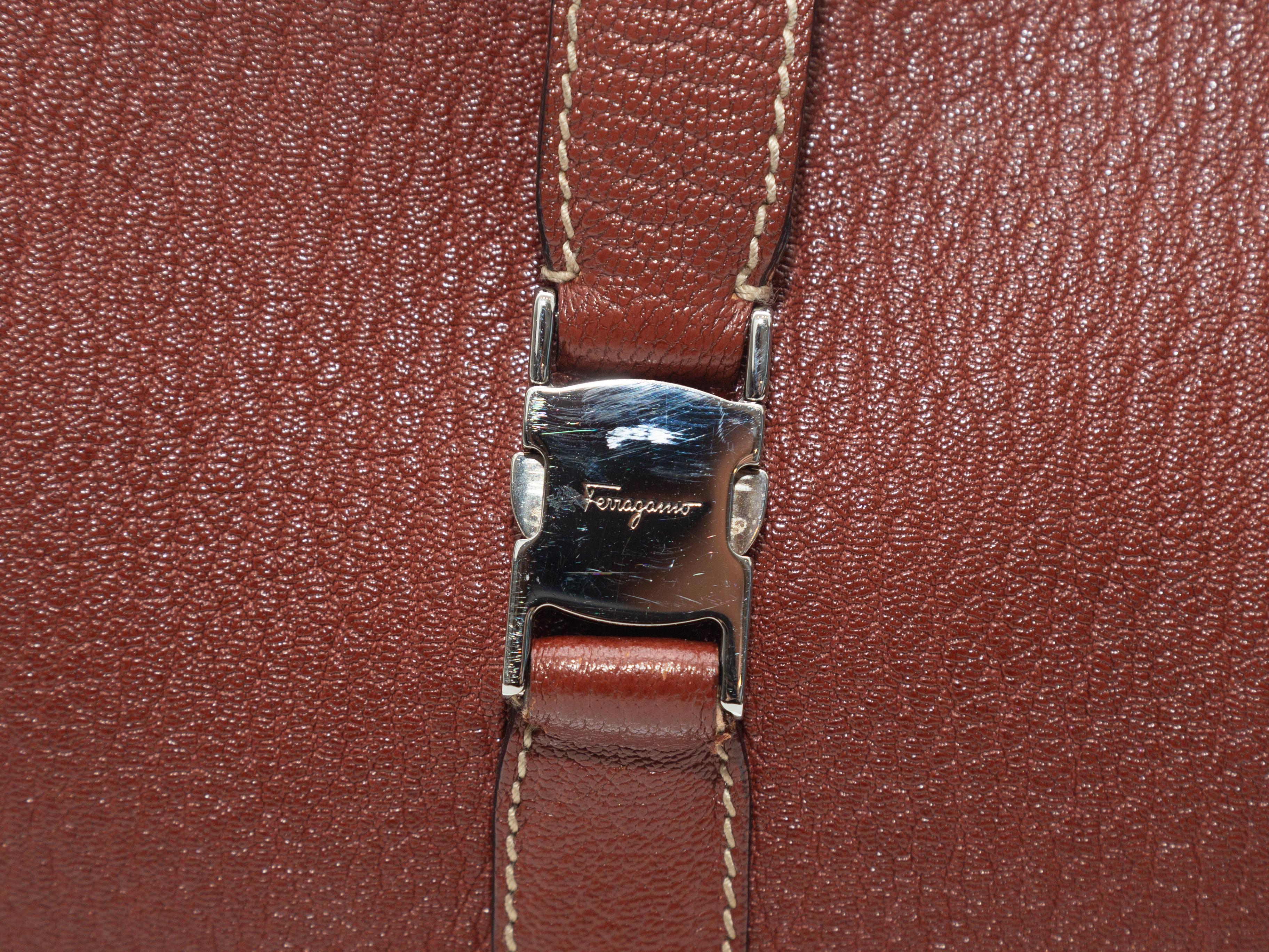 Product details: Brown leather shoulder bag by Salvatore Ferragamo. Silver-tone hardware. Contrast stitching throughout. Interior zip pocket. Buckle accent at front. Zip closure at top. 12