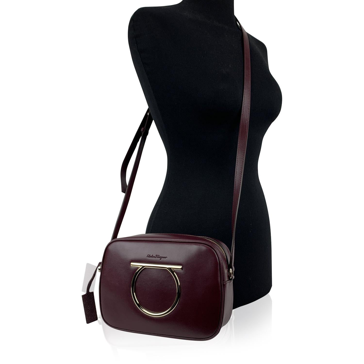 Beautiful 'Vela CC' shoulder bag by Salvatore Ferragamo. Made of burgundy calf leather. It features the Gancino logo detailing on the front in gold metal. Upper zipper closure. Adjustable leather shoulder strap. Canvas lining. 2 side open pockets