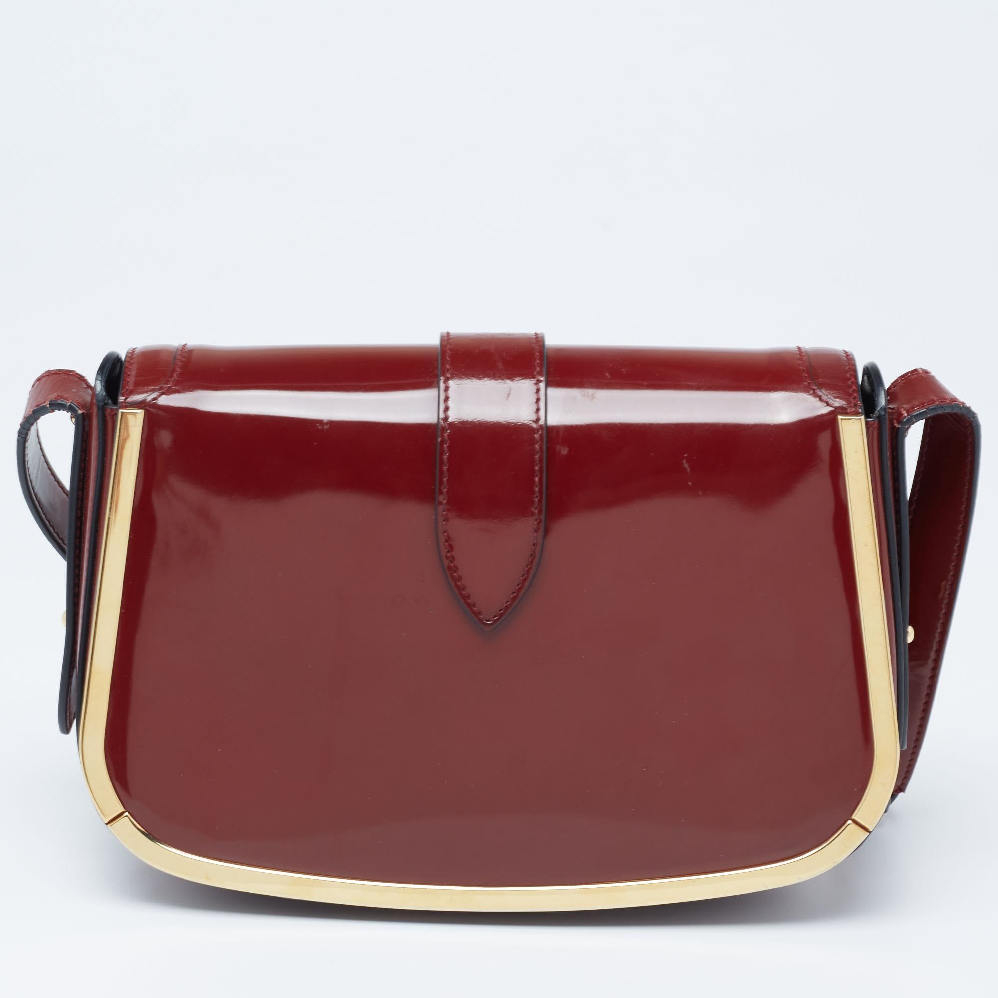The gold-tone accents enhance the appeal of this Salvatore Ferragamo bag. Made in a classy burgundy hue, this patent leather creation is made functional with a shoulder strap and a leather-lined interior. The Gancini design on the front offers it an